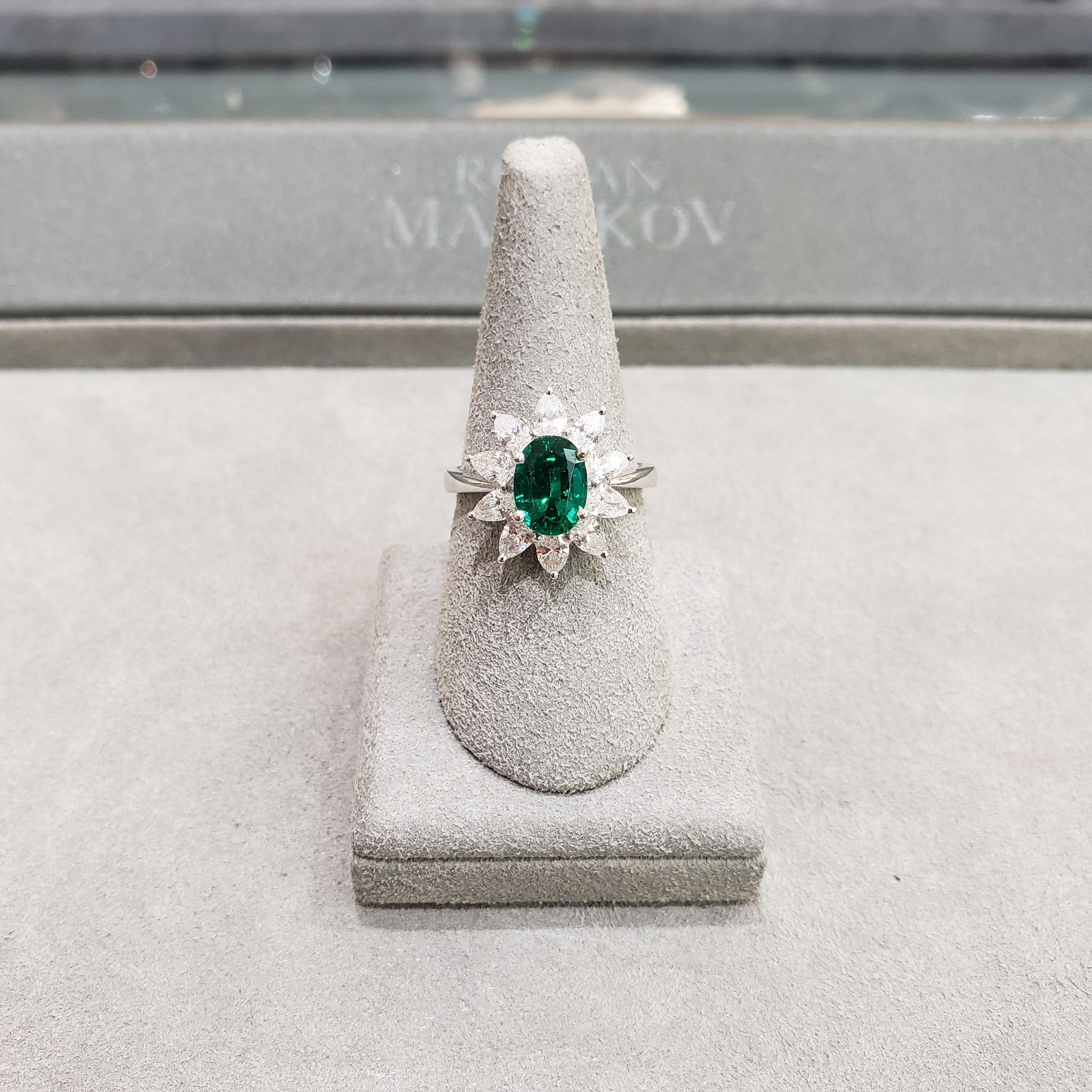 A stunning engagement ring, showcasing a color-rich 1.48 carats oval cut green emerald that is elegantly framed by 10 sparkling pear-shape diamonds of 1.06 carats total in a floral motif style. Mounted in solid 18K white gold. Size 6.5 US, resizable