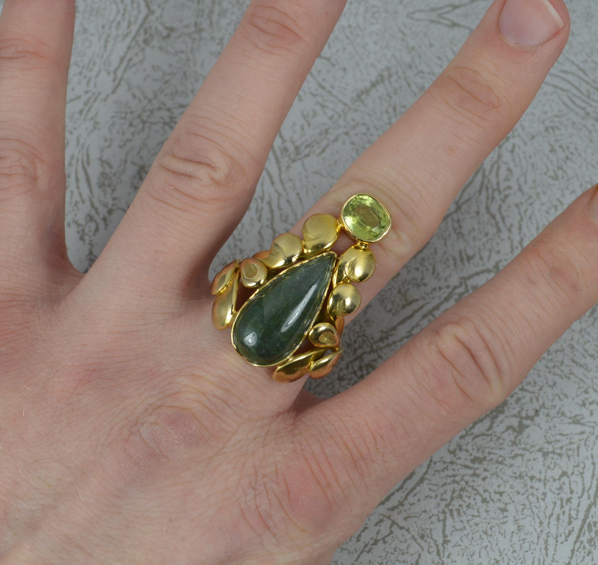 A superb art nouveau influenced ring.
Solid 14 carat yellow gold example.
Designed with a large 11mm x 23mm green tourmaline cabochon to centre with oval peridot set above and a fine gold floral leaf pattern to the sides.
The floral pattern then