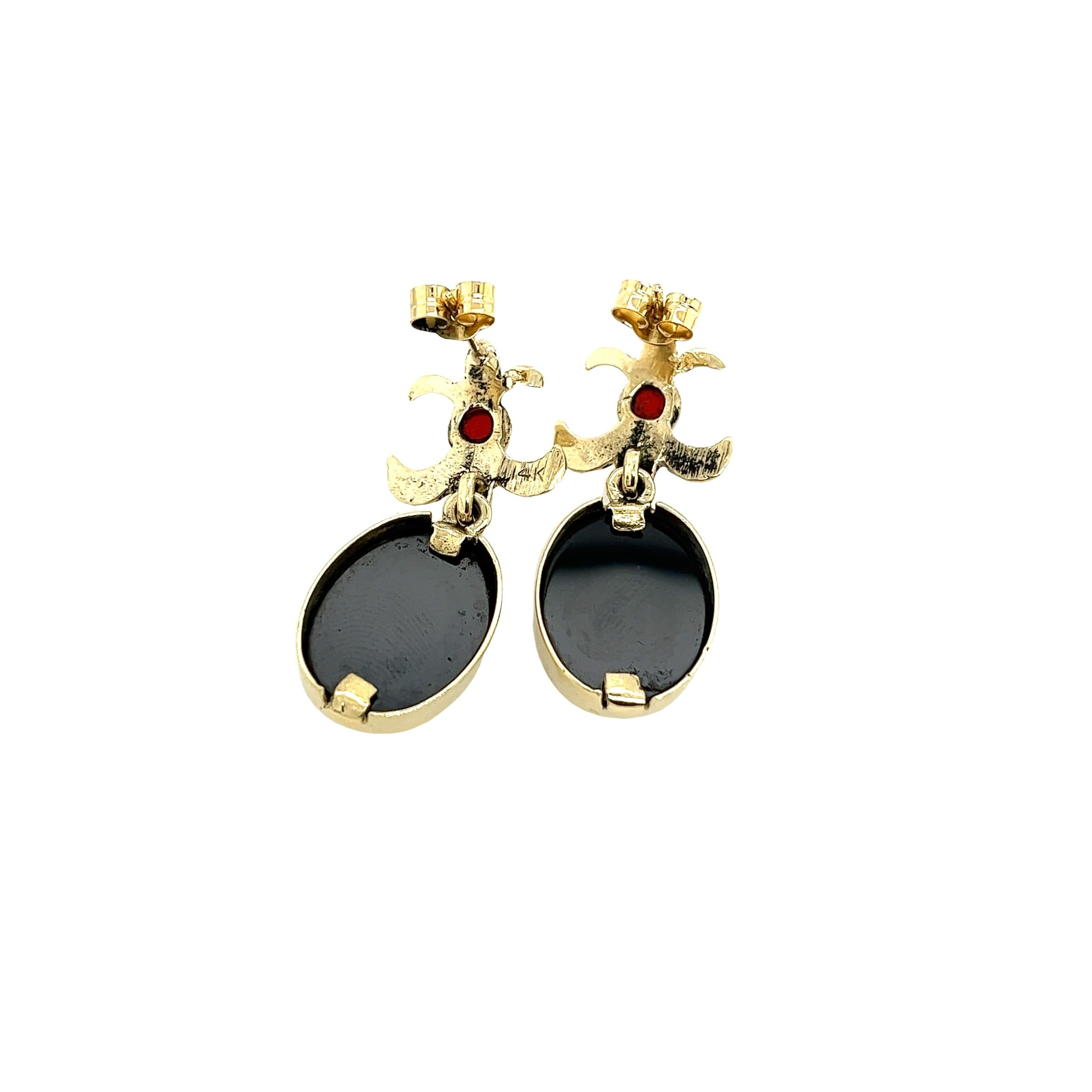 This vintage pair of drop earrings are made with 2 hematite carved onyx & 2 cabochon natural garnets,
They are mounted in 14ct yellow gold. 
Total Weight: 6.3g 
Earrings Dimension: 32mm x 13mm
Peg & Screw Fittings
SMS8622