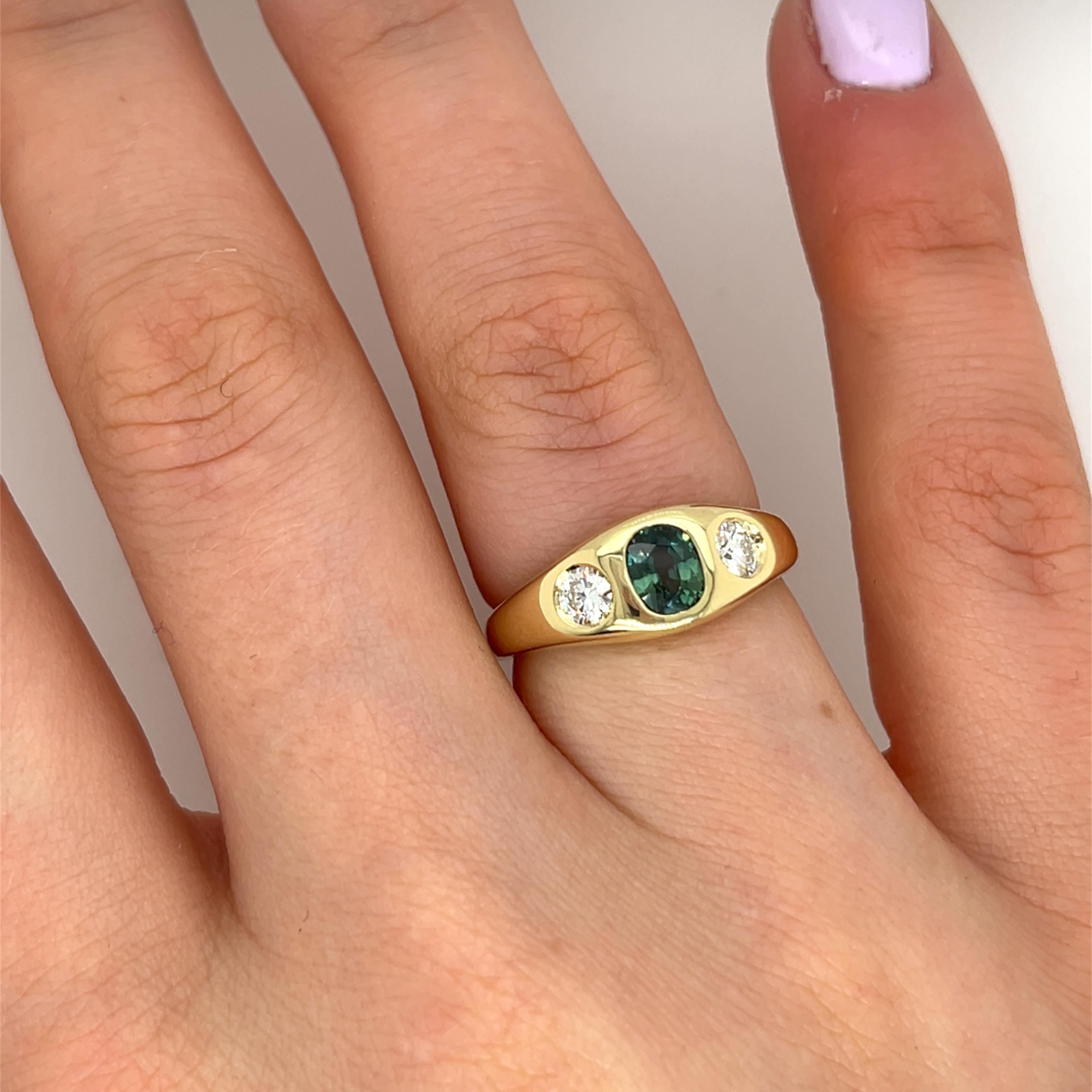 Magnifique bague en or jaune 14ct, ornée d'un saphir vert naturel de 0,75ct au centre, élégamment flanqué de deux diamants ronds de taille brillant dans une monture à chaton classique. Une pièce intemporelle et sophistiquée, 
parfait pour les