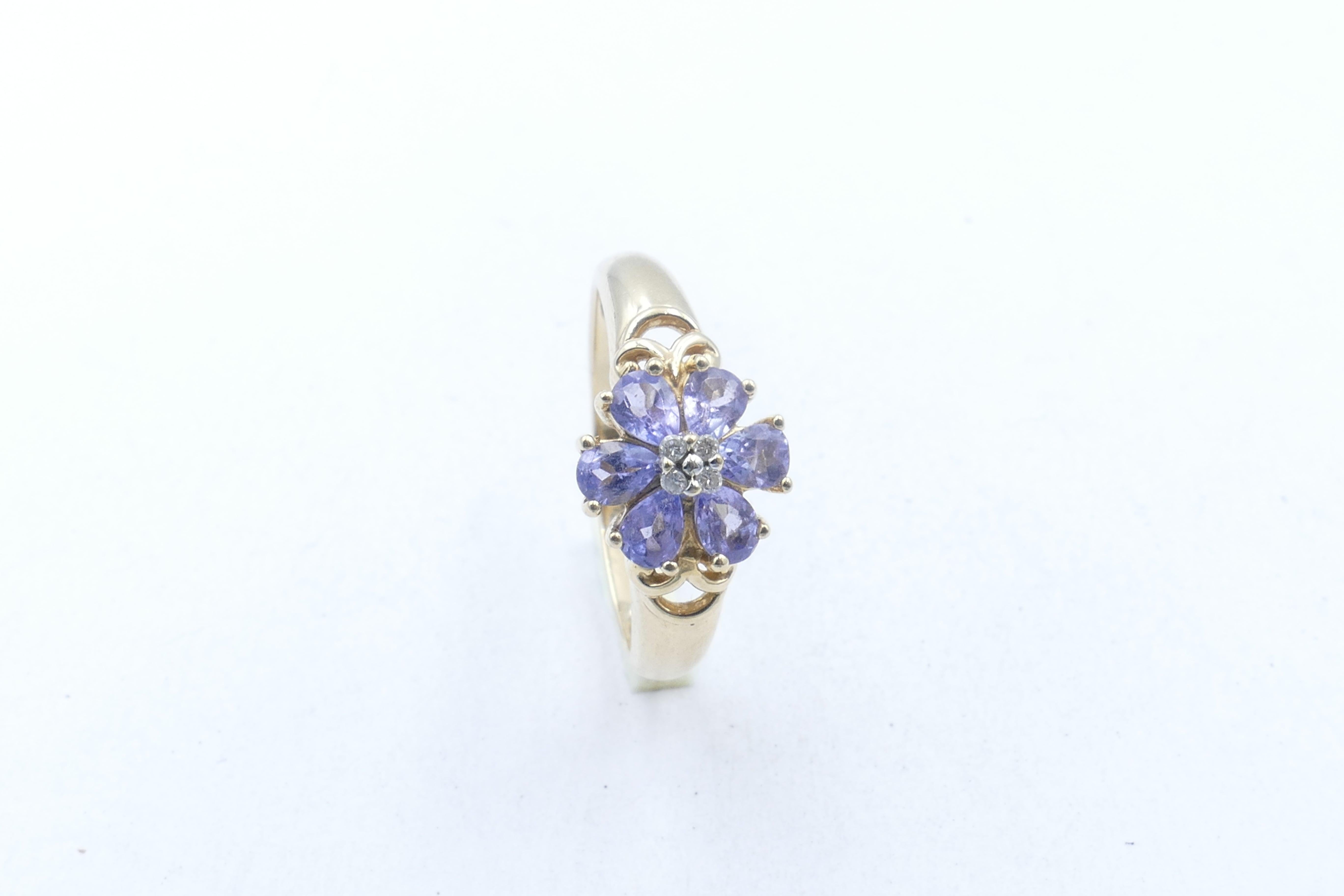 6 bluish-purple Tanzanites, pear cut, eye-clean & claw set  make up the 'Flower' petals.
4 Brilliant Cut Diamonds, claw set in white gold feature in the centre.
It is a very pretty Ring.
The band is polished, half round to a basket underrail &