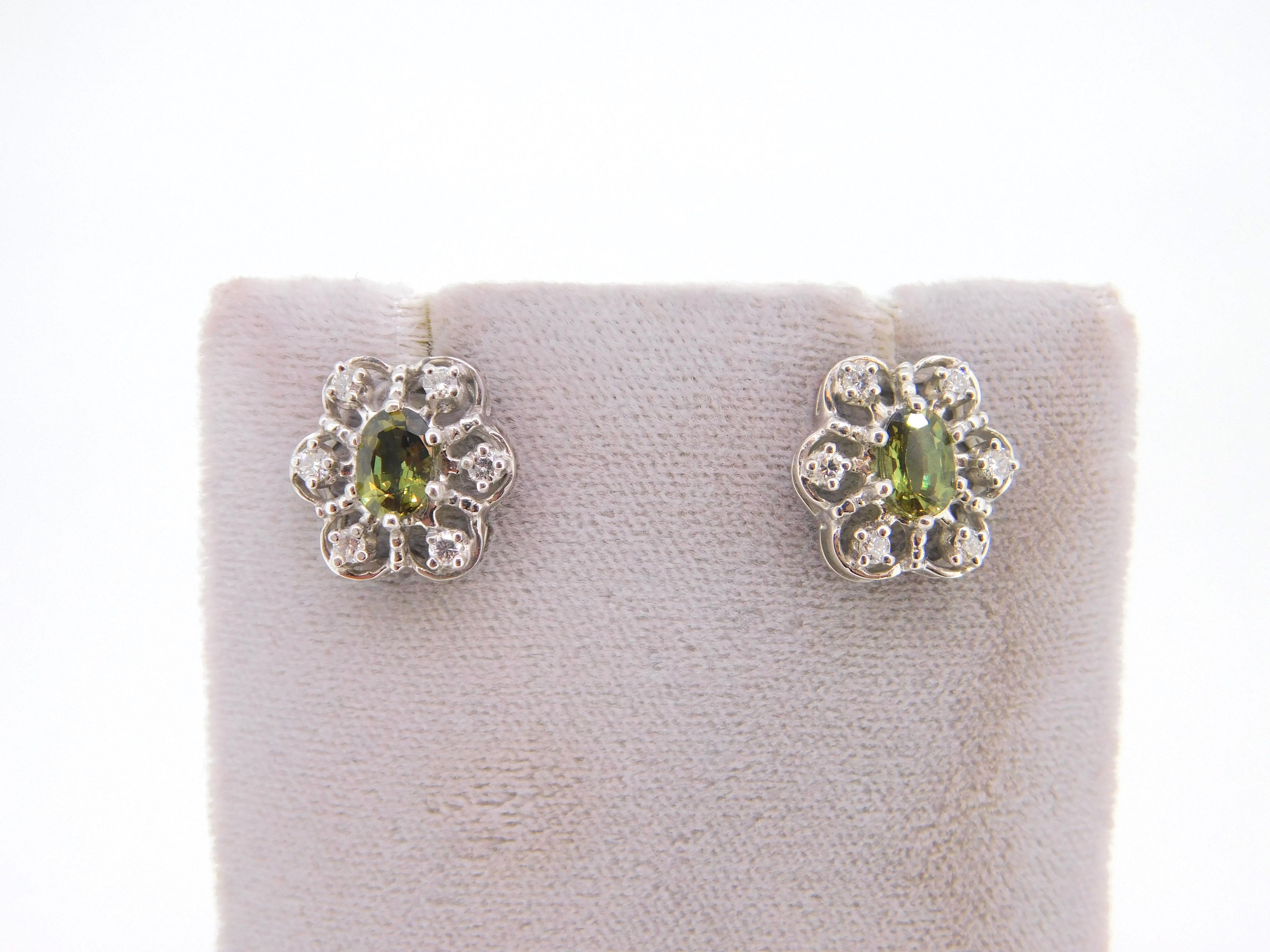 14K white gold natural alexandrite and diamond earrings. The oval natural alexandrites weigh 1.60 carats total and measure approximately 7mm x 5mm. The stones have a color change from purplish-brown to yellowish-green. There are 12 small round