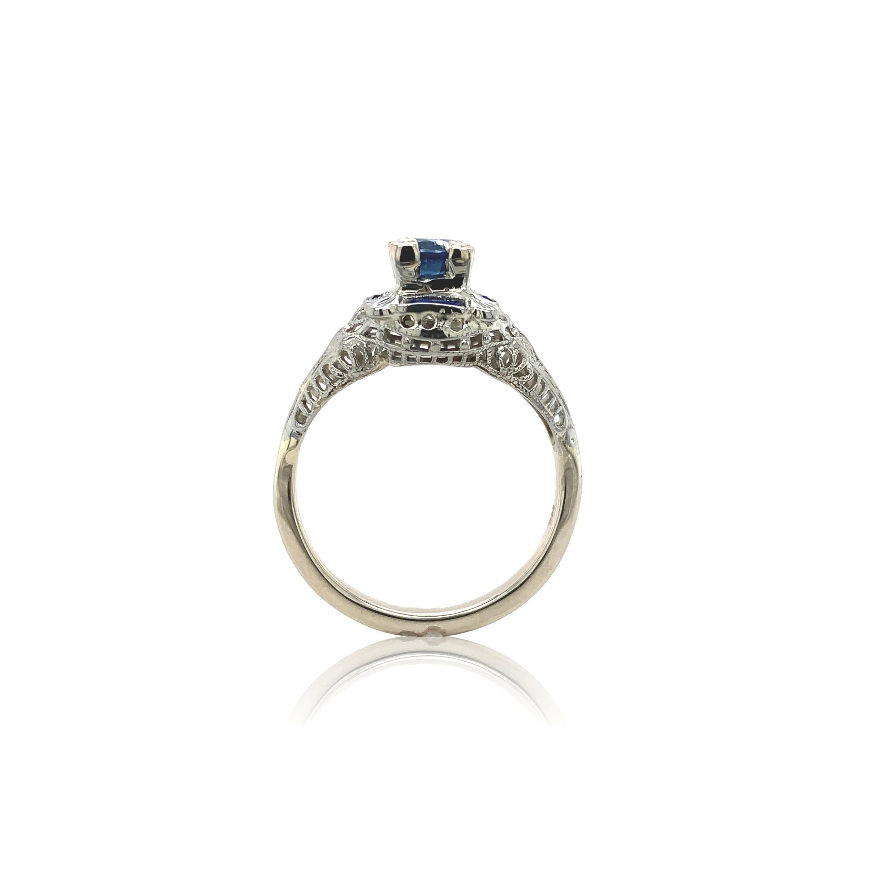 Bague Art déco en or blanc 14K filigrané, ornée d'un saphir bleu rond. Le saphir authentique extrait de la terre a une couleur bleu moyen. Le saphir mesure environ 4,8 mm et pèse 0,57ct. Le saphir est placé en hauteur et présente une certaine usure.