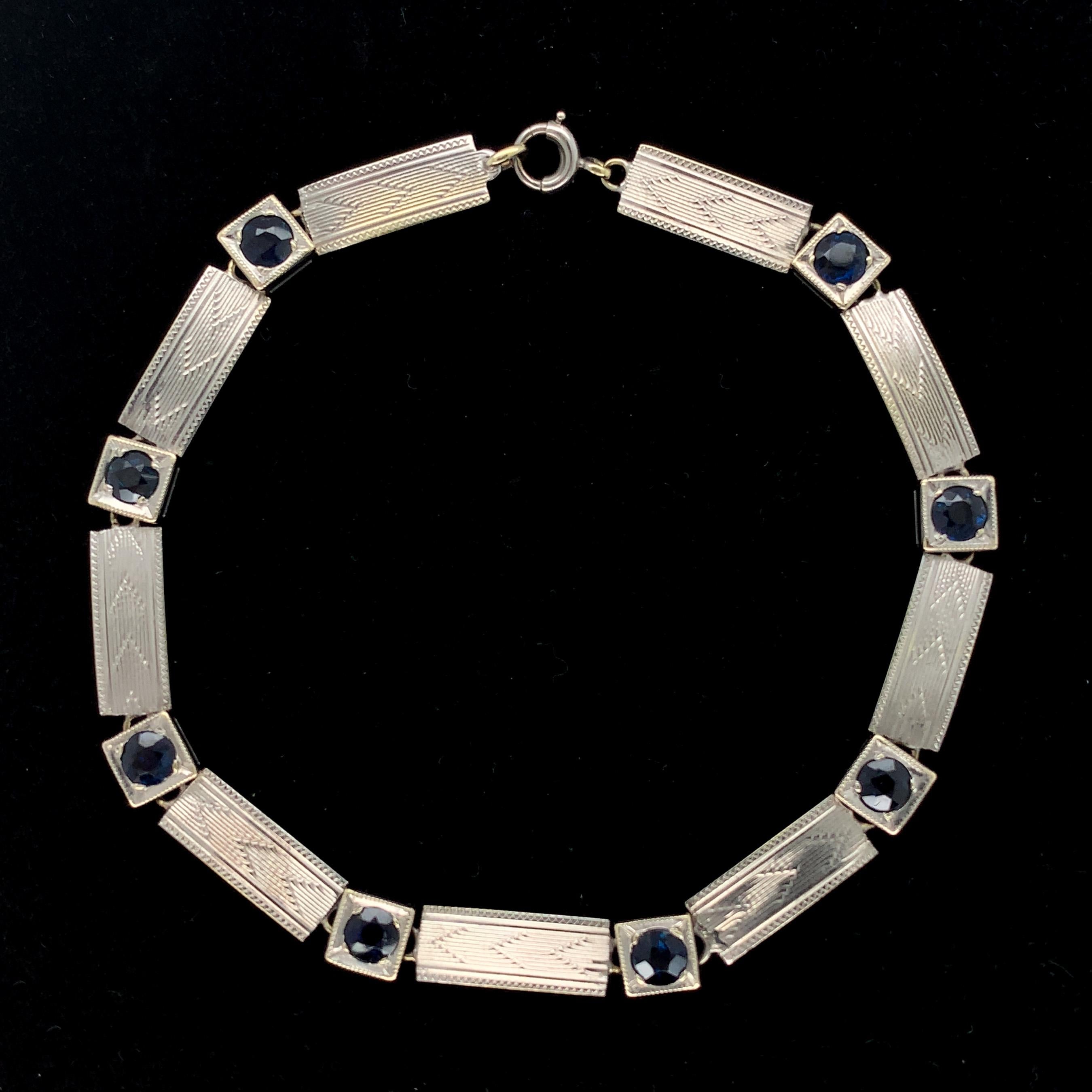 14K white gold bracelet with rectangular flat links with guilloche engraved design and round sapphires. There are 8 blue earth mined sapphires measuring about 3mm diameter. The unmarked bracelet tests 14K with a platinum top. The bracelet measures 7