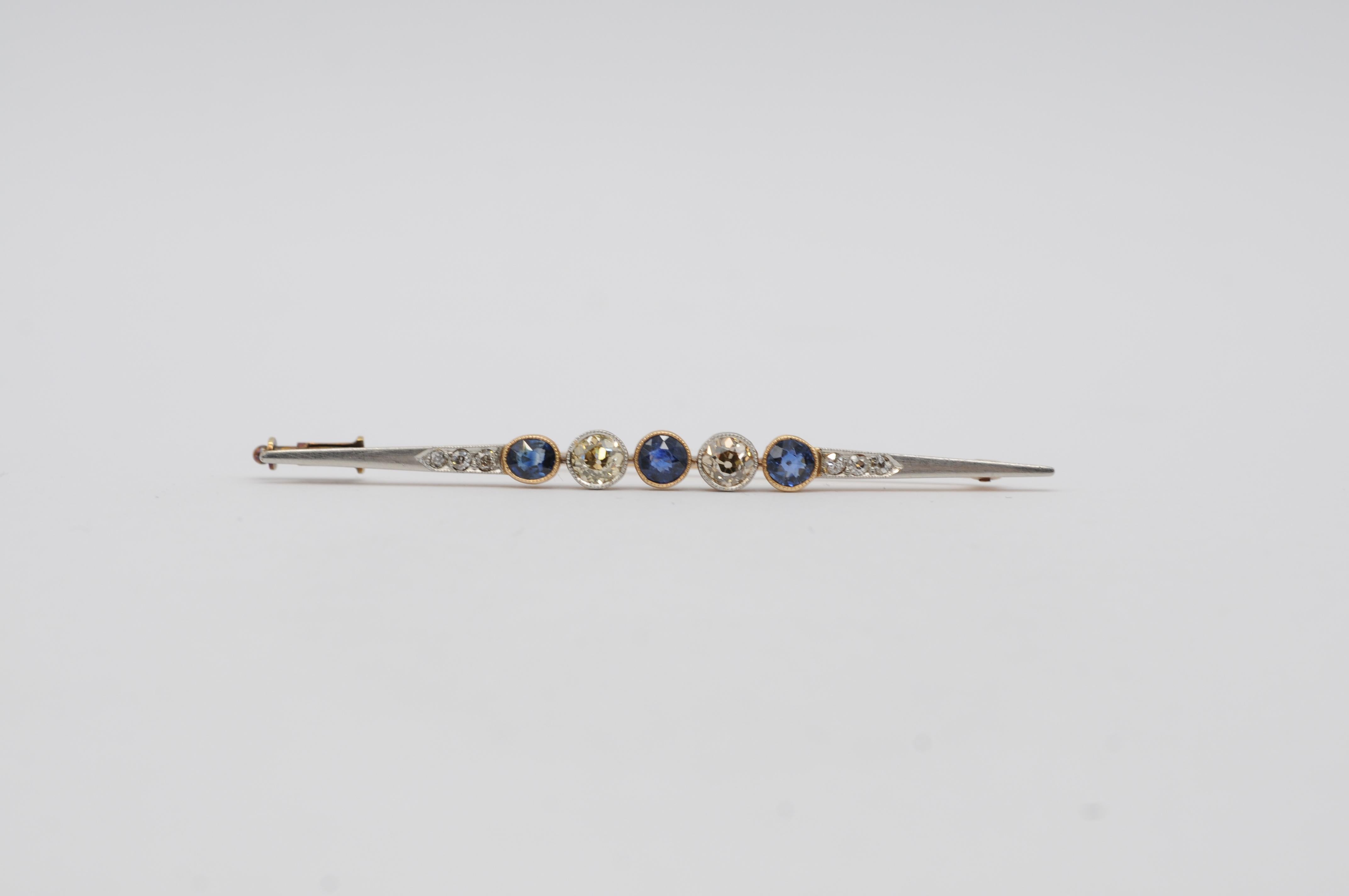 Este precioso broche Art Decó de 14 quilates en forma de bastón muestra una impresionante disposición de piedras preciosas naturales, que encarna la elegancia y sofisticación del periodo Art Decó. El broche presenta dos deslumbrantes diamantes y