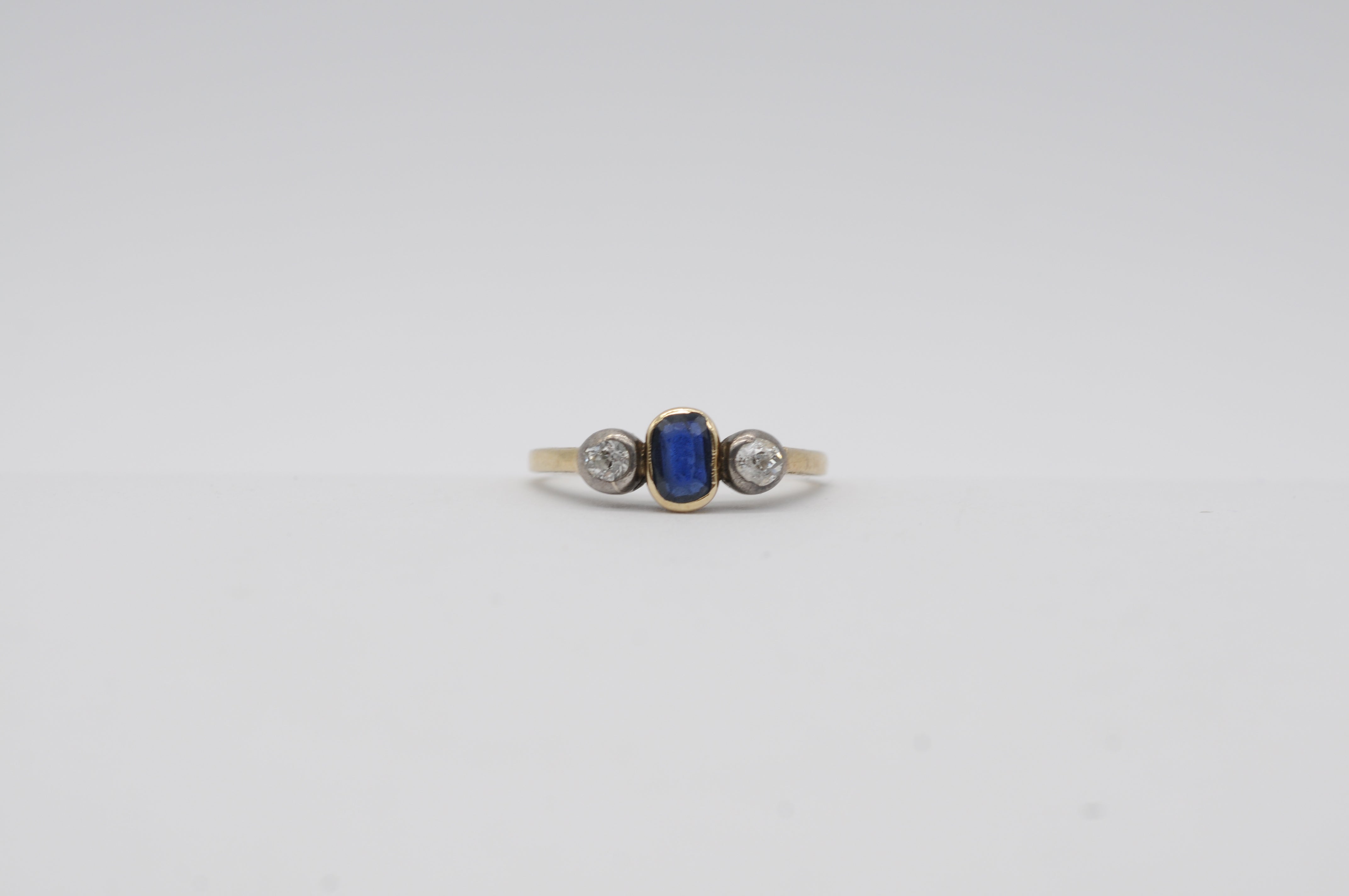 Dieser exquisite 14-karätige Art-Déco-Ring mit drei Steinen aus klassischem Gelbgold besticht durch einen natürlichen Saphir in der Mitte, der in tiefem Blau strahlt. Der Saphir wird auf jeder Seite von zwei funkelnden Diamanten mit einem Gewicht