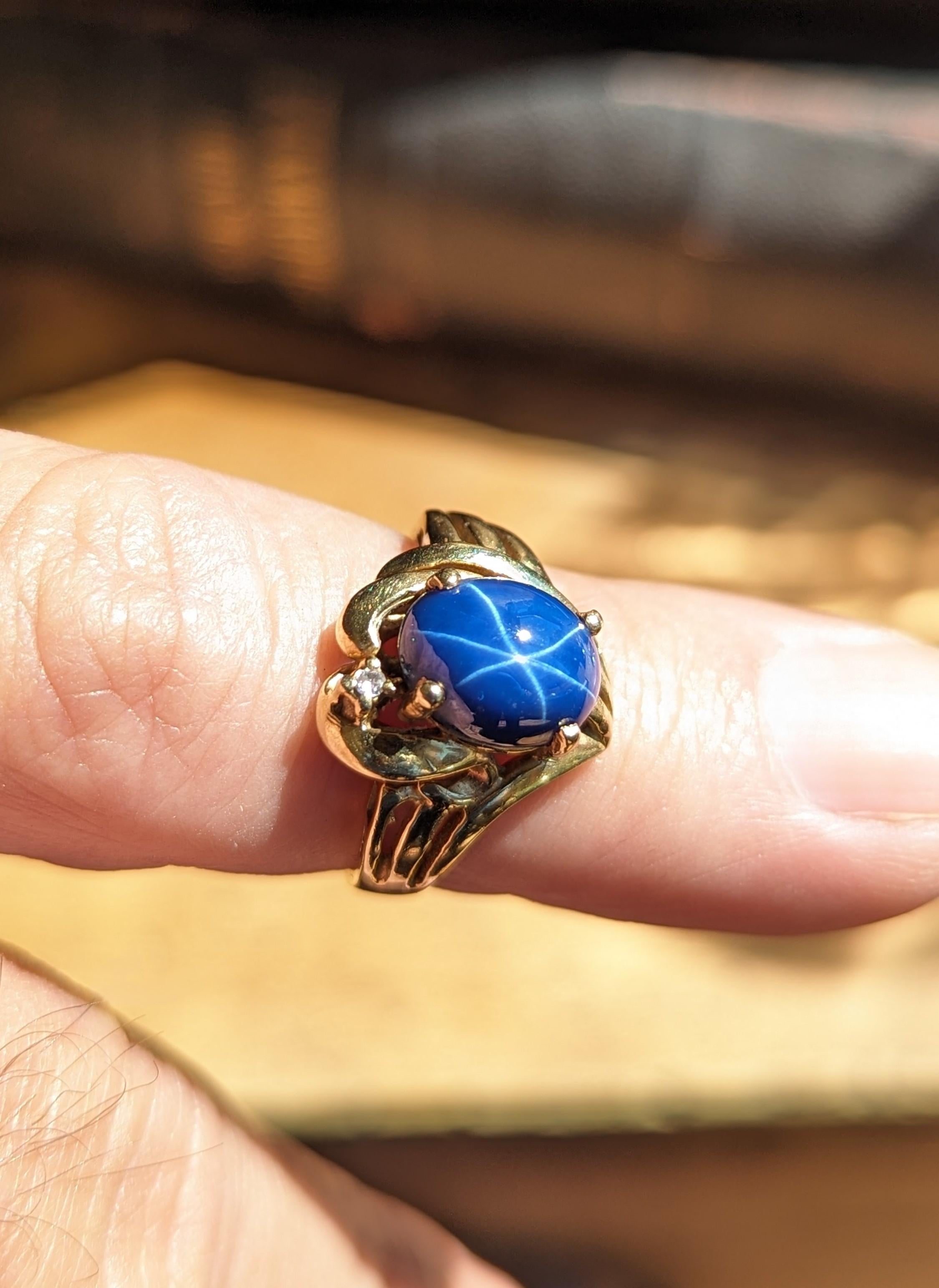 Elegant vintage blue star sapphire ring set in solid 14k yellow gold featuring a diamond accent. Open work metal with a flowing ribbon design, best fits for a size 6.25 finger. Measures 14.5mm at its tallest points by 2.8mm at its smallest points,
