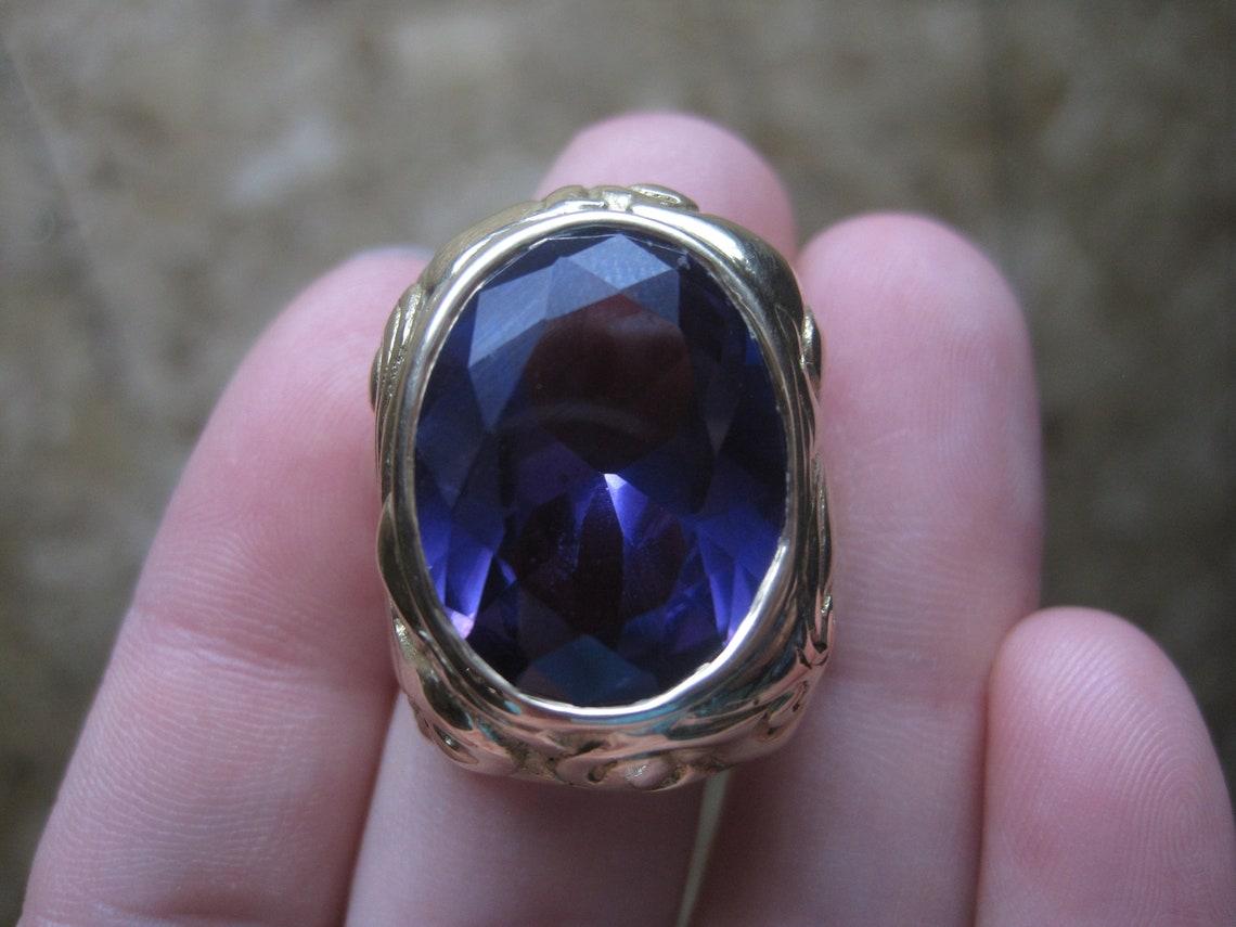 Questo splendido anello, unico nel suo genere, è grande e carico.
È enorme!

Questo anello è in oro giallo 14k.
Presenta una pietra di alessandrite sintetica color change di 16x20 mm con taglio ovale.
Passa dal viola al rosso e, con alcune luci, può