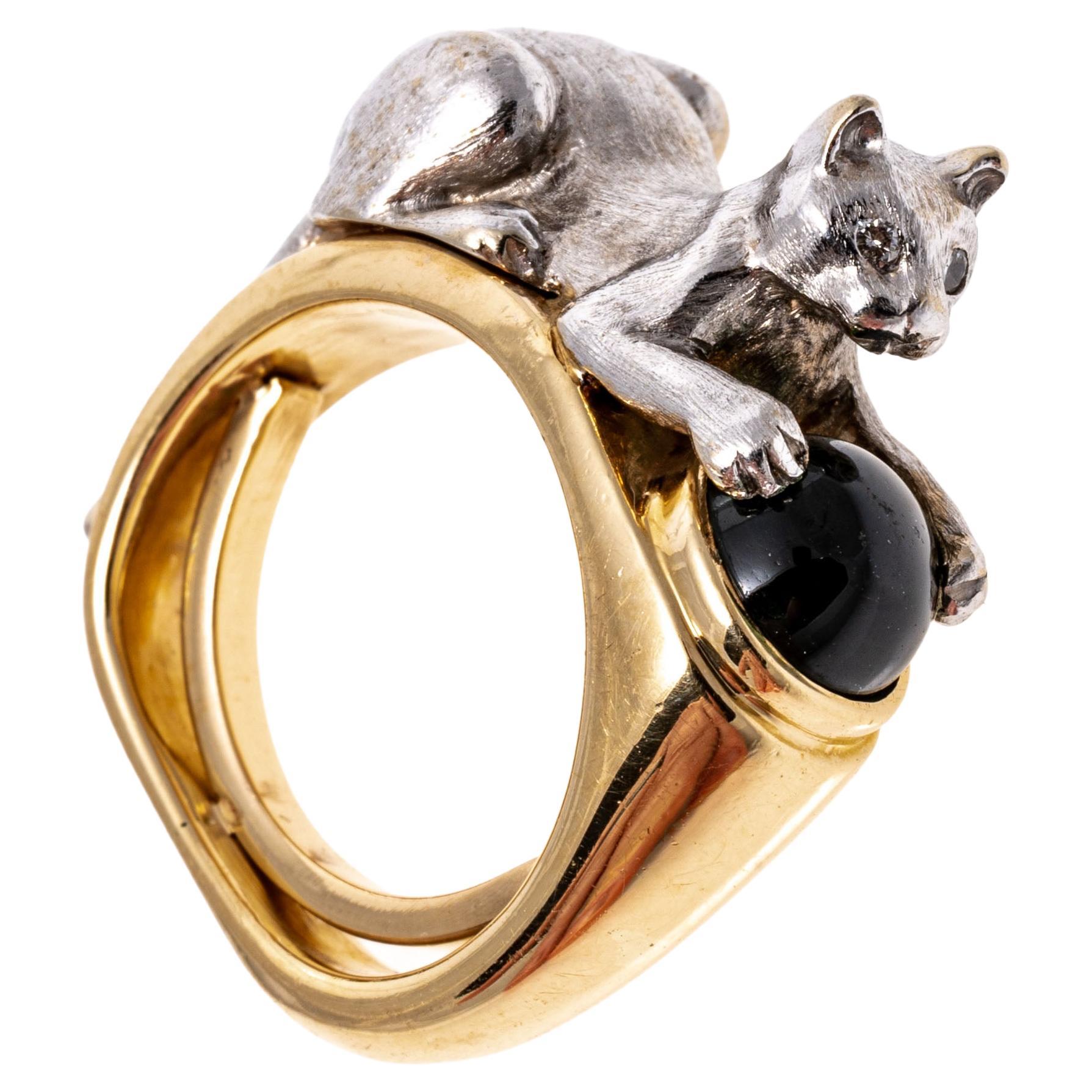 14K white and yellow gold ring. A playful white gold cat with a brushed finish crouches over the yellow gold band. Set between the cat's front paws is a deep green chrome diopside with cabochon cut. The cat's eyes are set with bright round cut