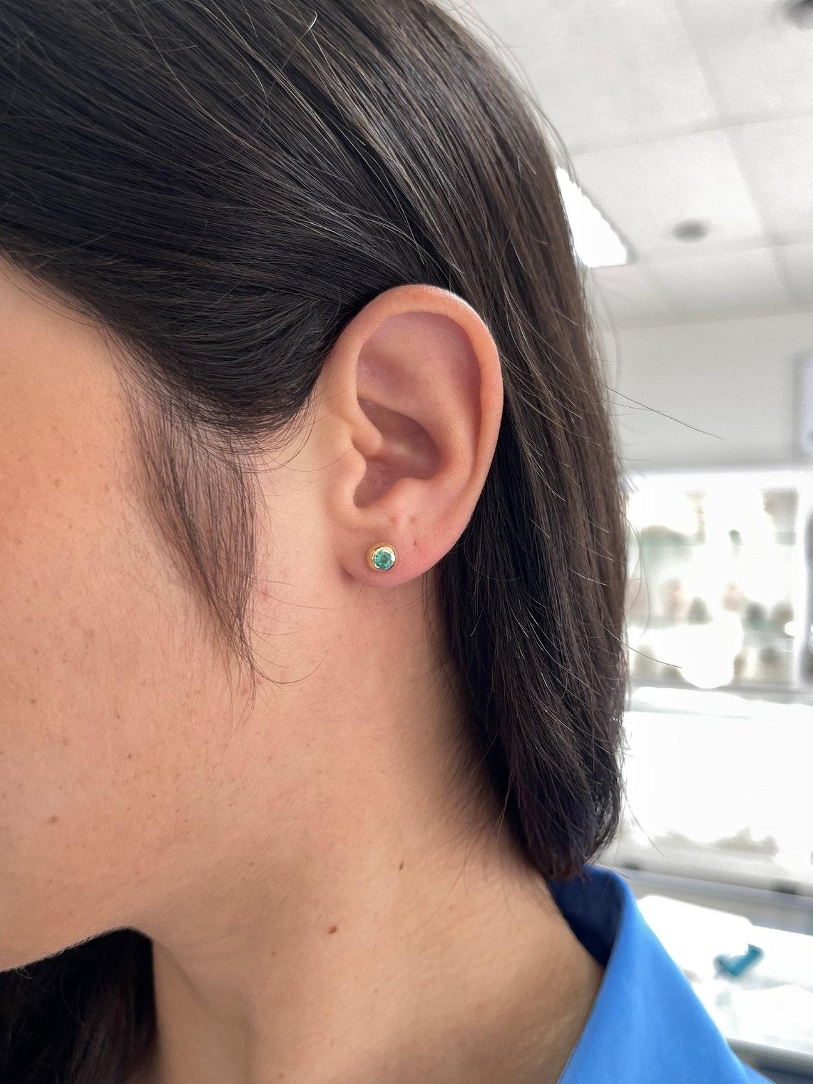 Entdecken Sie die Eleganz in ihrer einfachsten Form mit unseren Petite Emerald Stud Earrings. Diese exquisiten Ohrringe präsentieren zwei bezaubernde Smaragde im Rundschliff, von denen jeder einen fesselnden mittelgrünen Farbton und einen