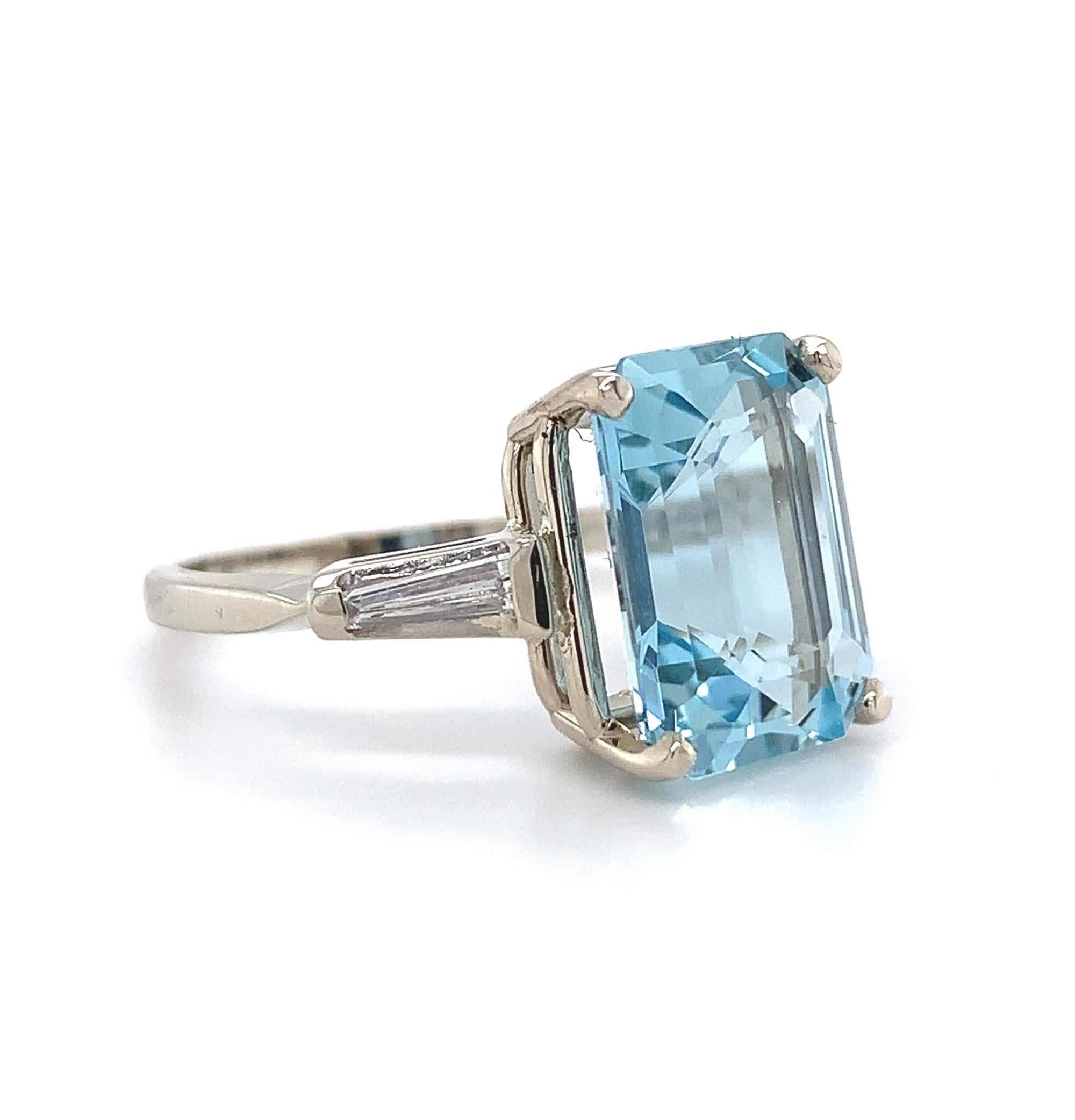 14K white gold aquamarine and diamond ring featuring an emerald cut aquamarine weighing 4.51 carats. The aqua has sky blue color and fine clarity. It measures about 12 mm x 9mm. The aqua is accented by 2 long tapered baguette diamonds weighing about
