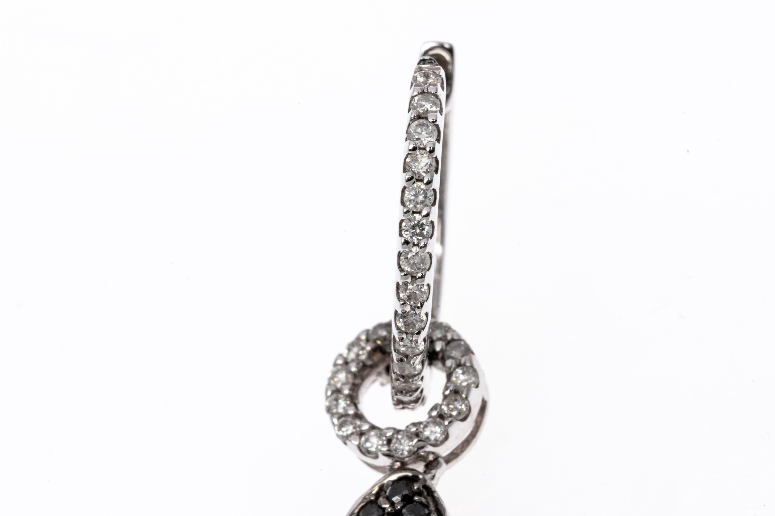 14k white gold earrings. These fabulous earrings contain a small hoop top, set with a row of round faceted, white diamonds. Suspended from the hoop is a pear shaped open drop style pendant, bordered with a scalloped edge of round faceted black