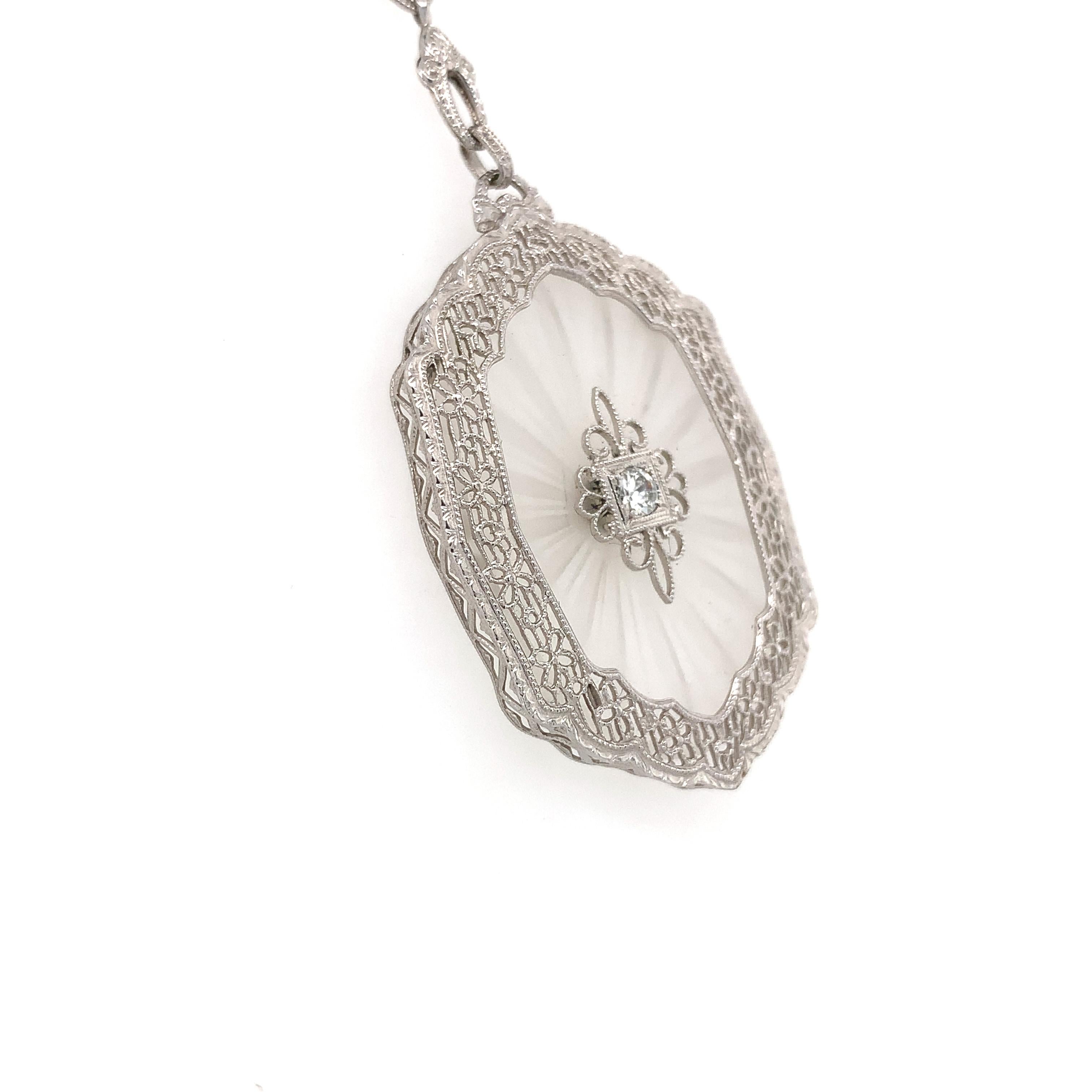 Art Deco 14K white gold necklace featuring a large beautiful frosted and reverse carved rock crystal quartz panel. The large oval crystal measures about 30mm x 22mm, and is accented with a small round diamond measuring about 2.5mm. There is a wide