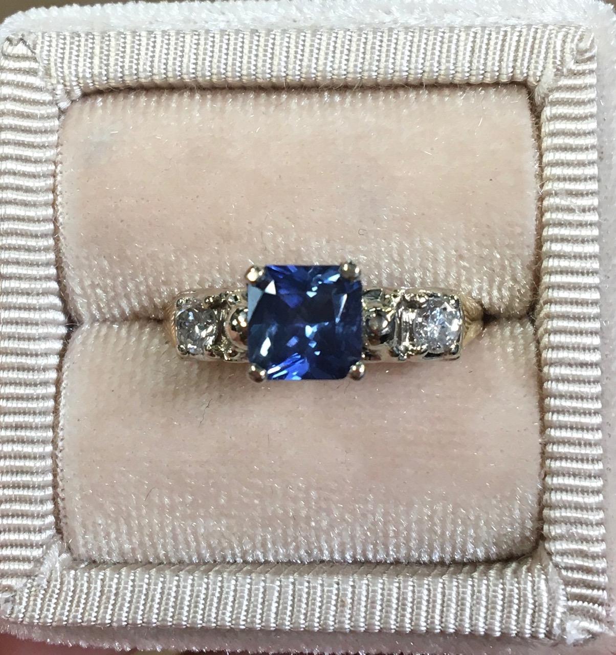 14K yellow and white gold blue sapphire and diamond ring. The ring features a square princess cut earth mined blue sapphire weighing 1.32 carats. There are 2 round brilliant cut diamond accents measuring about 3mm and weighing about .20cts total.