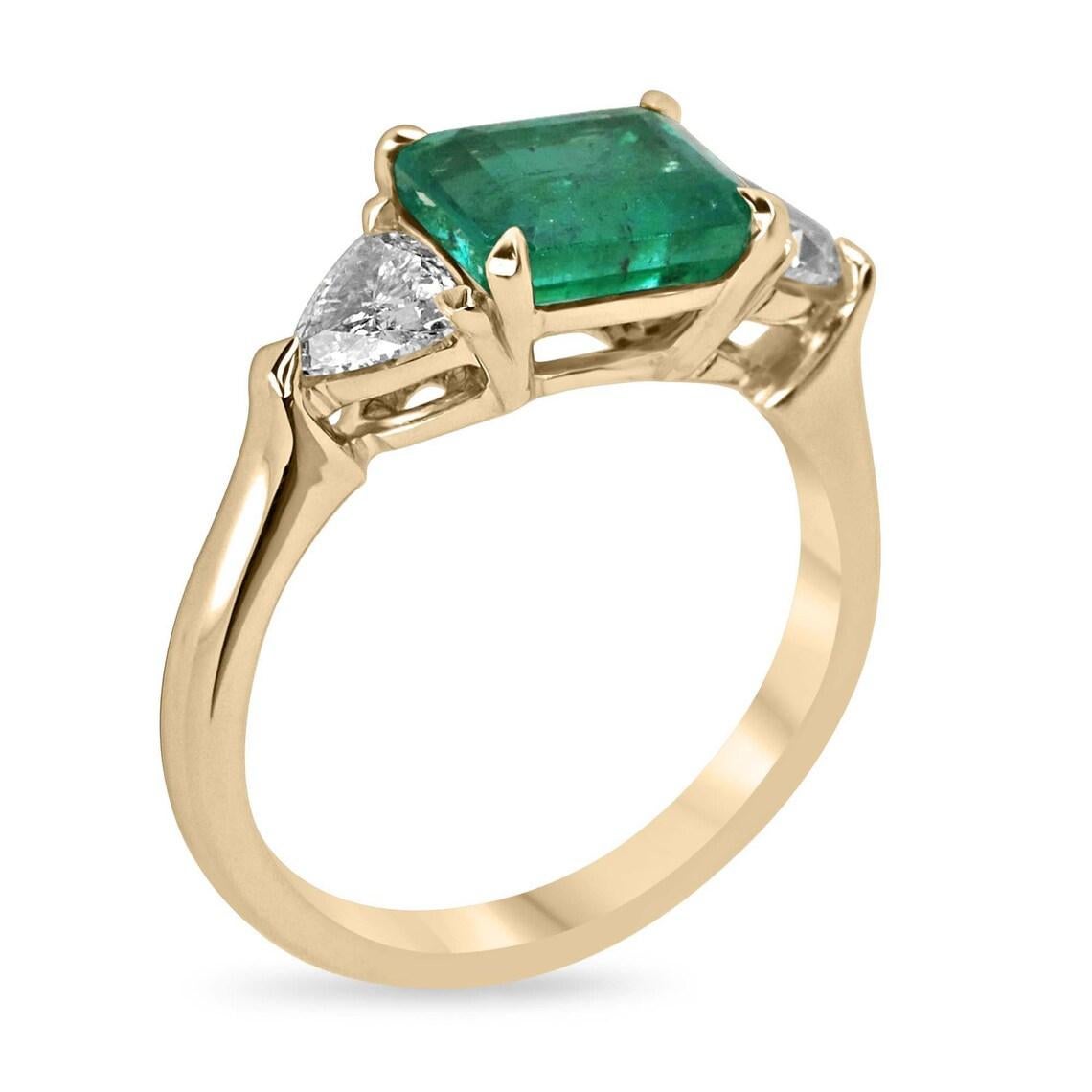 Eleva tu estilo con este exquisito anillo de tres piedras de esmeralda y diamantes. El centro del escenario lo adorna una cautivadora esmeralda de 1,92 quilates, de un exuberante color verde oscuro y muy buena claridad y brillo. Engarzada en una