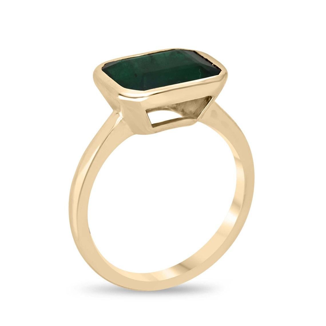 Elegance meets eco-consciousness in our Solitaire Emerald Ring, featuring a captivating east-to-west emerald cut emerald. This naturally sourced gem boasts a rich, dark forest green hue and semi-transparent clarity, providing a vivid connection to