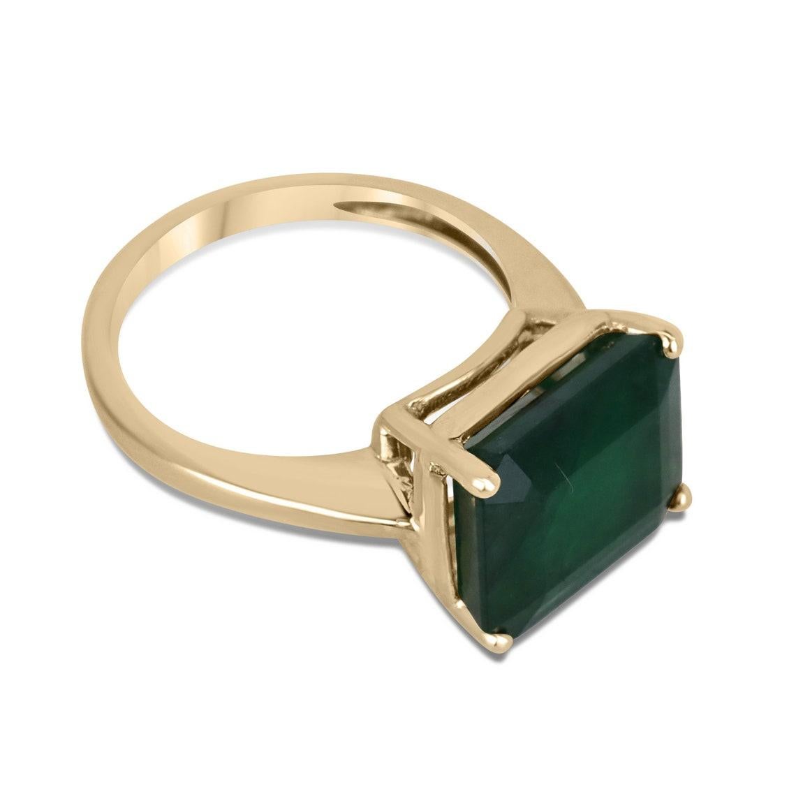 This elegant solitaire ring showcases a magnificent 6.28 carat emerald cut emerald, which is set east to west to accentuate its classic shape. The emerald boasts a rich, dark green color that exudes natural beauty and is set in a secure four-prong