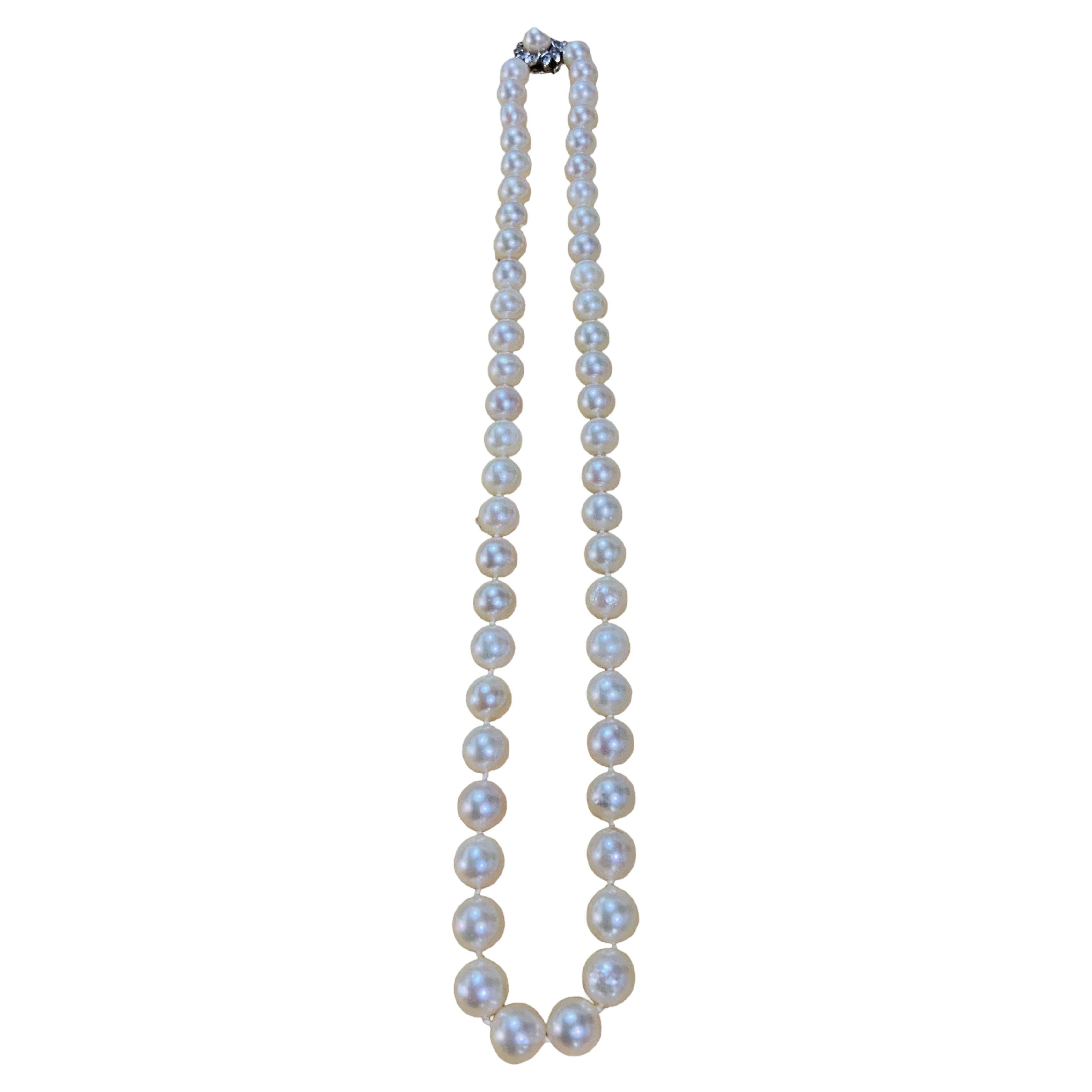 This is a 14K White Gold Akoya Pearls and Diamonds necklace. It depicts a necklace made of round pearls spheres fasten on a silk string with double knots. Its 14k white gold hidden box safety closure is shaped as a flower adorned with a single pearl