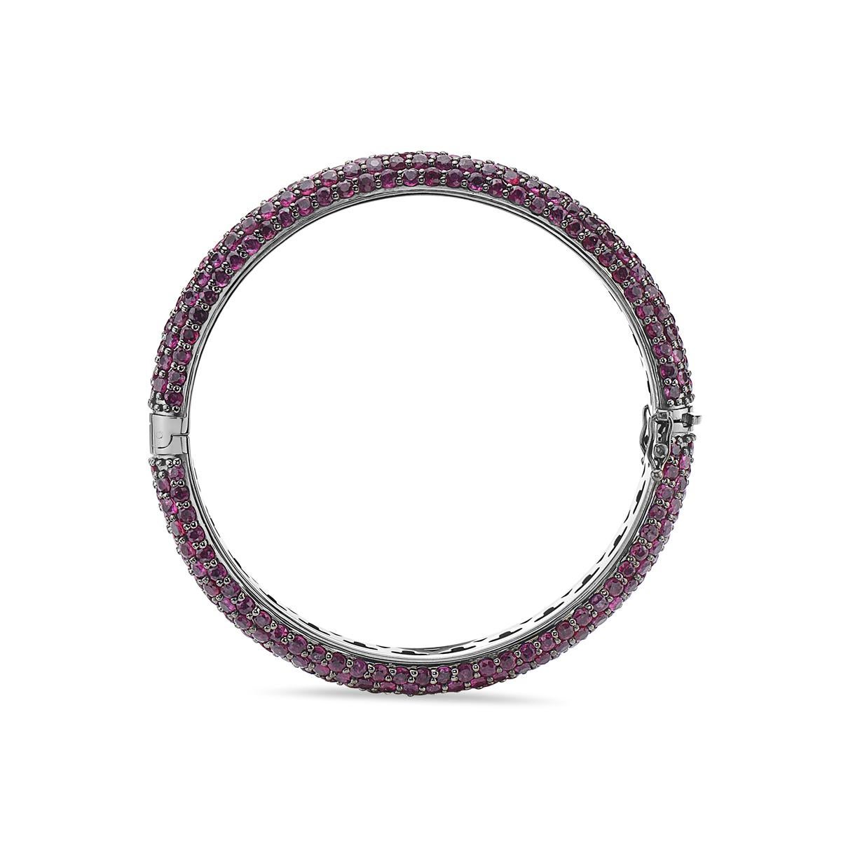 This bangle features 336 round cut rubies weighing 27.41 carats set in 14K gold that is coated in black rhodium. Measuring 2 3/8 inches in diameter and weighs 50 grams total weight. Features a double clasp closure.  