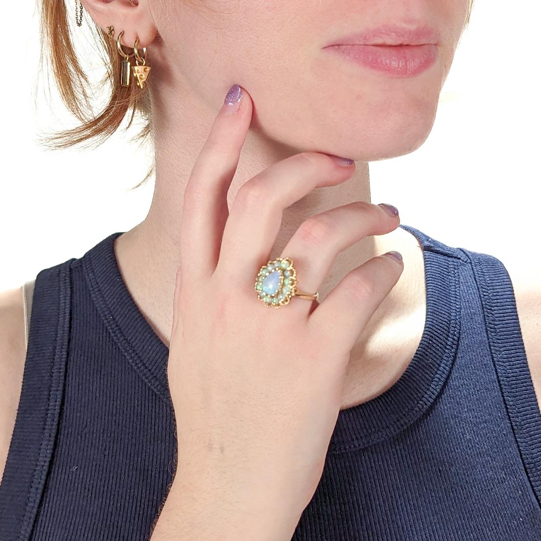 Un buen anillo de cóctel.

En oro amarillo de 14 quilates.

Engarzado en el centro con una gema de ópalo en forma de lágrima que está rodeada por un halo de ópalos redondos pulidos engastados con garras.

Marcado 14k en la caña.

¡Simplemente un