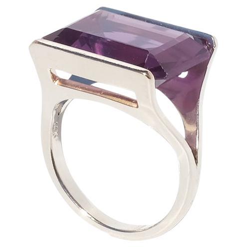 Dieser Vintage-Ring aus 14-karätigem Gold zeichnet sich durch einen auffälligen, rechteckigen synthetischen Korund in einem satten Violettton aus. Der Stein im Smaragdschliff ist in eine offene, geometrische Lünette gefasst, die den Pavillon