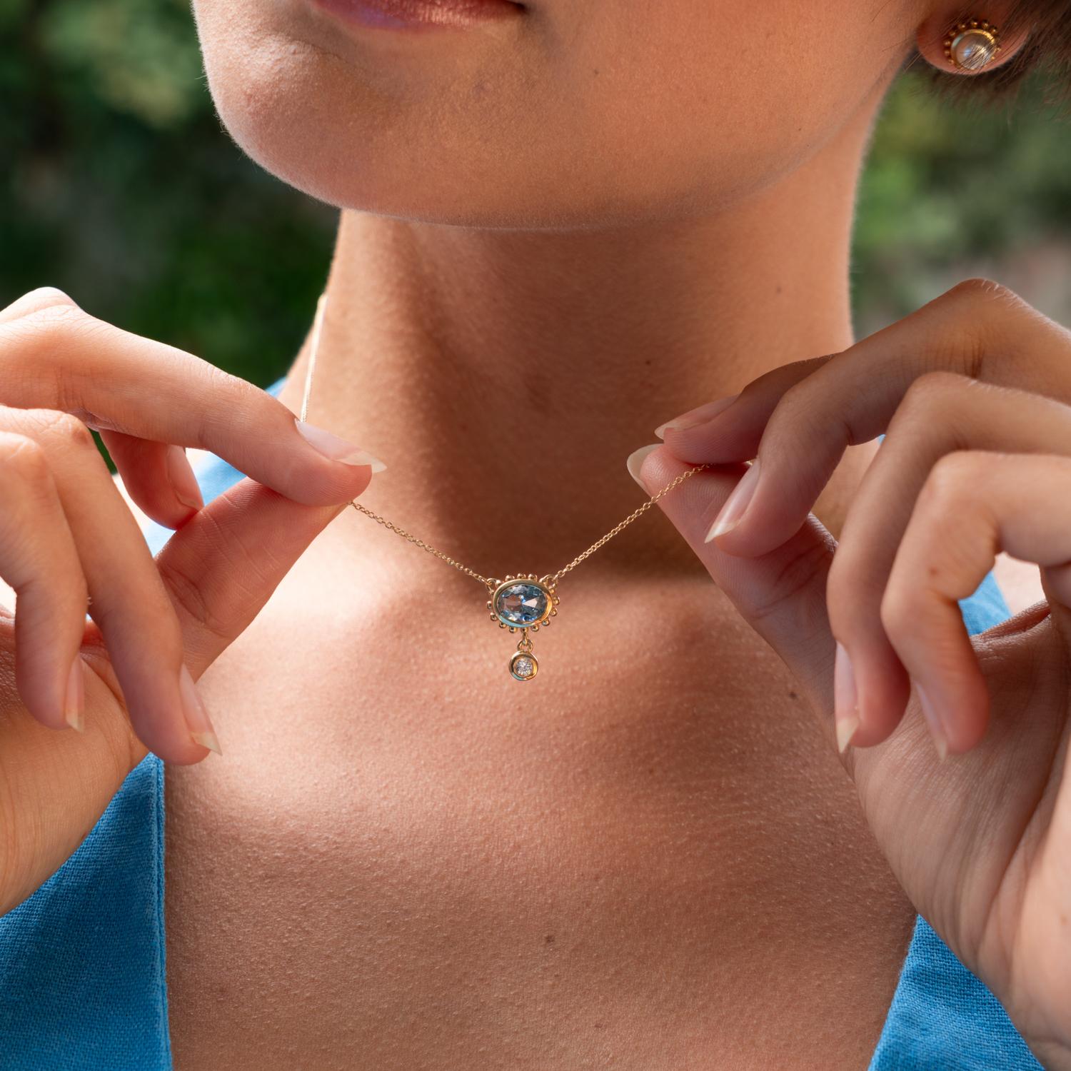 This elegant pendant is set with an oval blue topaz in solid 14k yellow gold. The handcrafted design features granulated spheres adorning the outside of the setting and is complete with a tiny diamond dangling beneath. Inspired by creatures of the