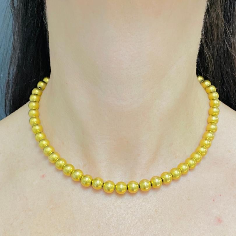 A shiny 14k gold bead necklace, circa 1970s.
The necklace comprises of evenly sized gold beads strung along a woven gold cord. The beads have a slightly matte finish rather than a high polish, giving the piece a more understated look. The