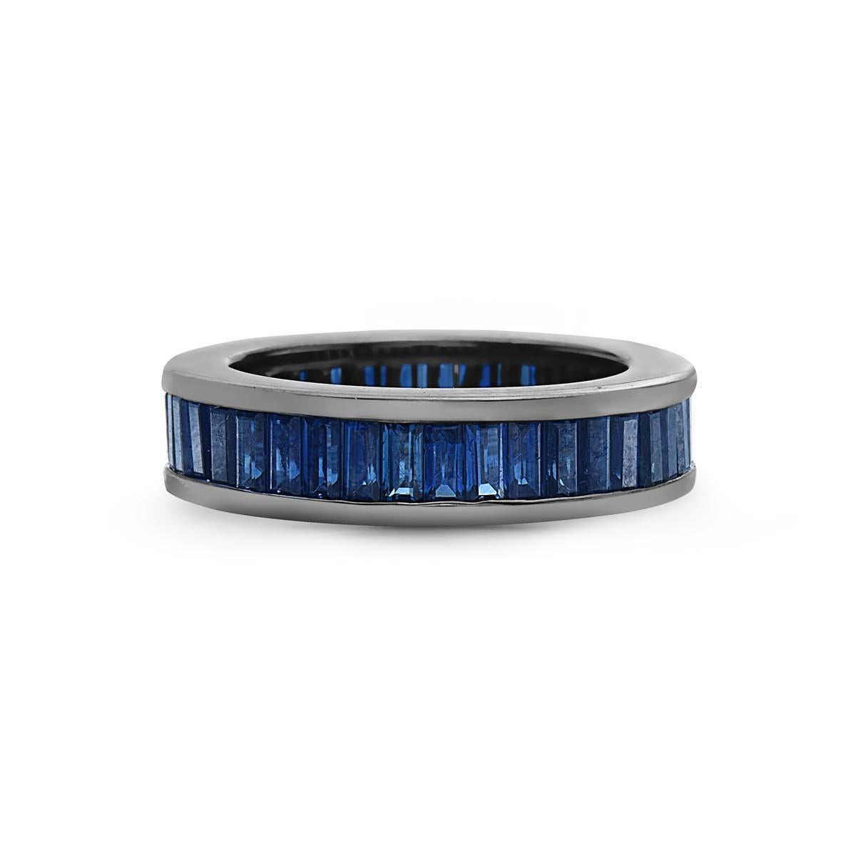 This eternity band ring features 40 baguette cut sapphires weighing 4.30 carats set in 14K gold dipped in rhodium. 6.1 grams total weight. Size 6.