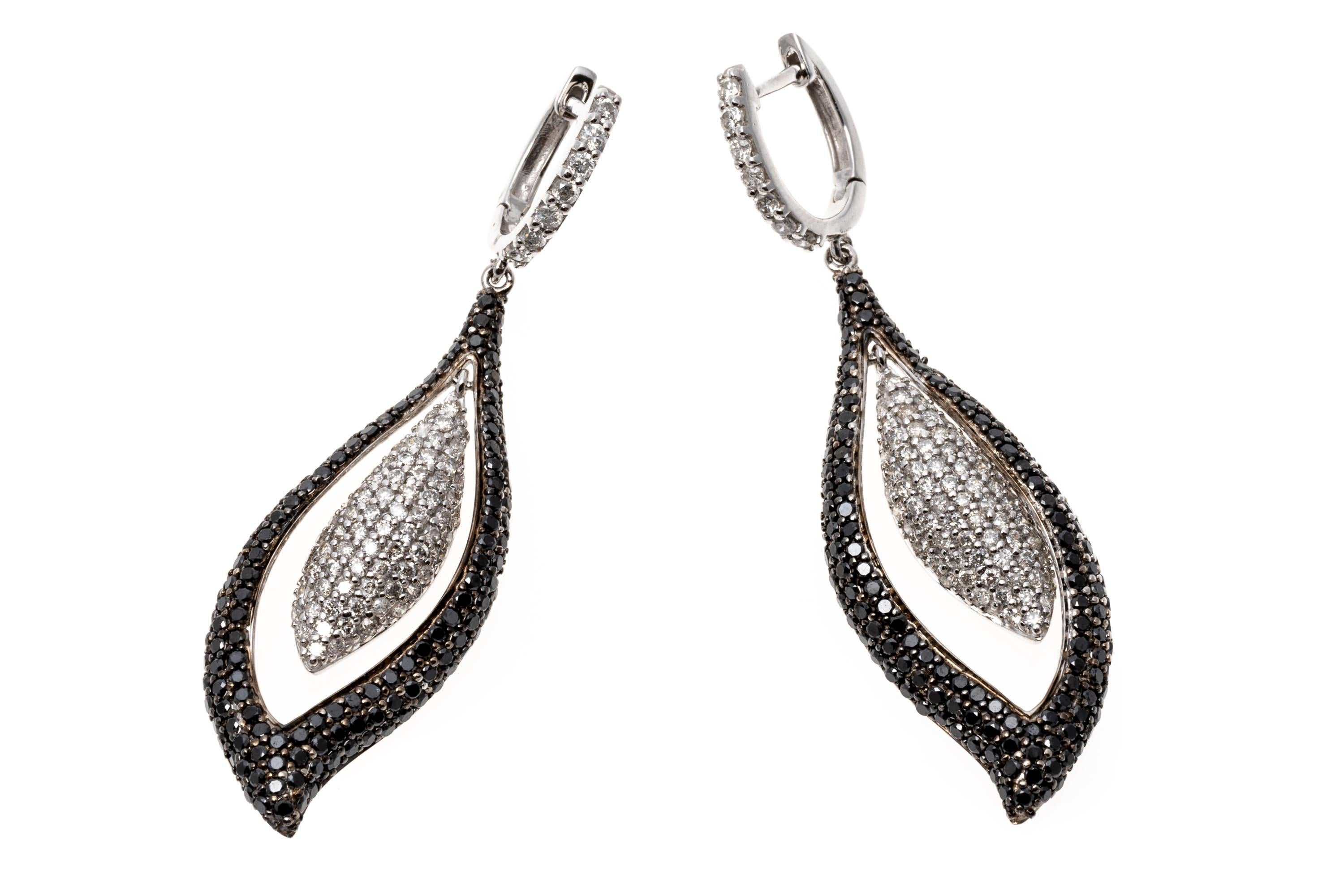 These brilliant 14K white gold earrings display an opposing design of leaf shaped pendants. The outer pendant is set with black diamonds while the inset one presents white diamonds creating an eye-catching contrast. The diamonds are approximately