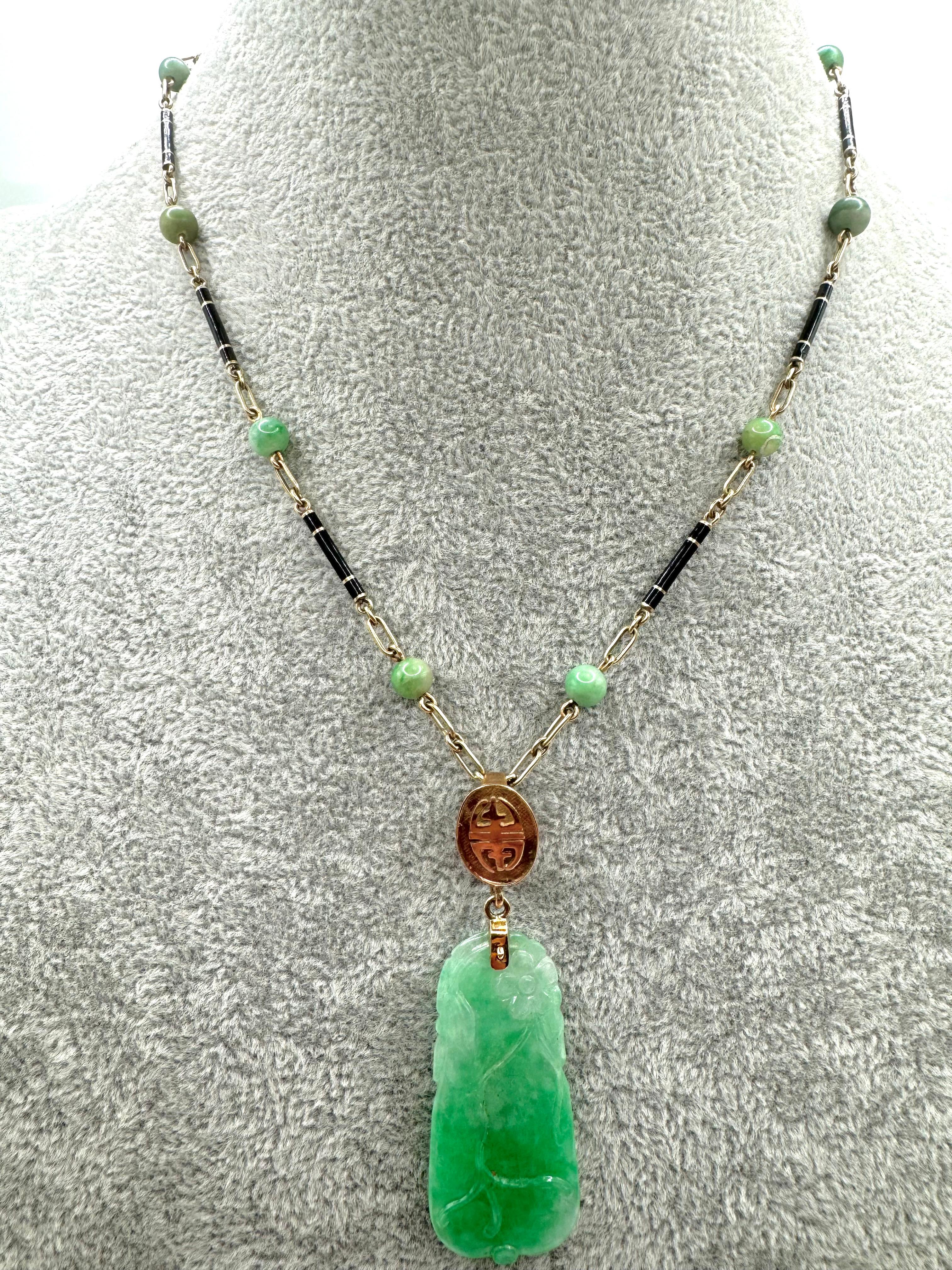 An elegant and culturally rich necklace crafted in 14 karat yellow gold, featuring a detailed hand-carved green jade pendant suspended from a finely constructed chain of alternating black enamel links and 10 smooth round jade beads. The central