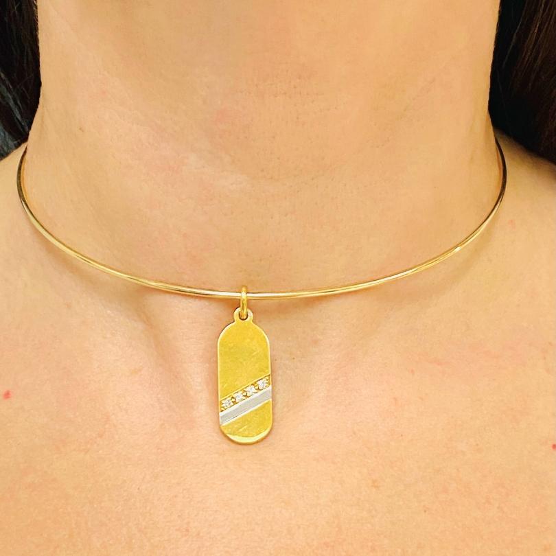 Una collana girocollo in oro 14k con un pendente di diamanti in oro 18k. u2028Il girocollo è minimalista, realizzato con un delicato filo d'oro che si appoggia con grazia al collo. Il ciondolo è un rettangolo piatto e allungato con angoli
