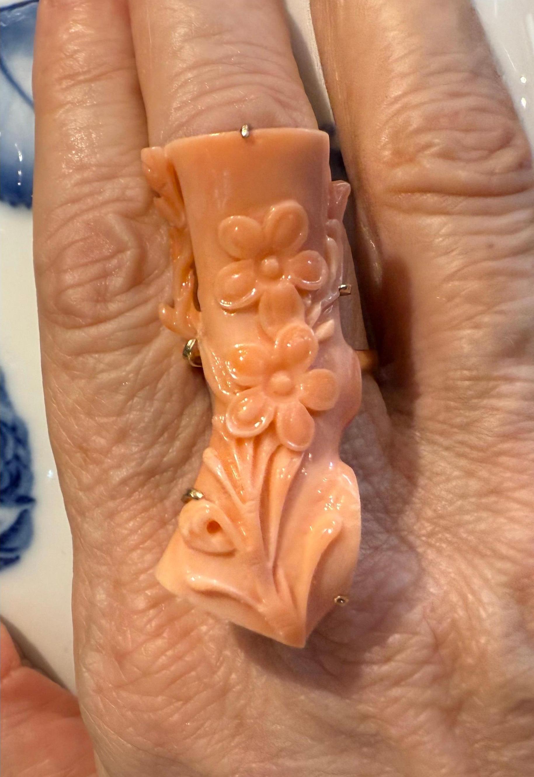 Questo è un anello di corallo in oro 14K. Raffigura un corallo simile a un tronco montato in una montatura d'oro. Il corallo è impreziosito da rami a voluta intagliati a mano e da due fiori. L'anello ha il marchio dell'oro 14 carati.