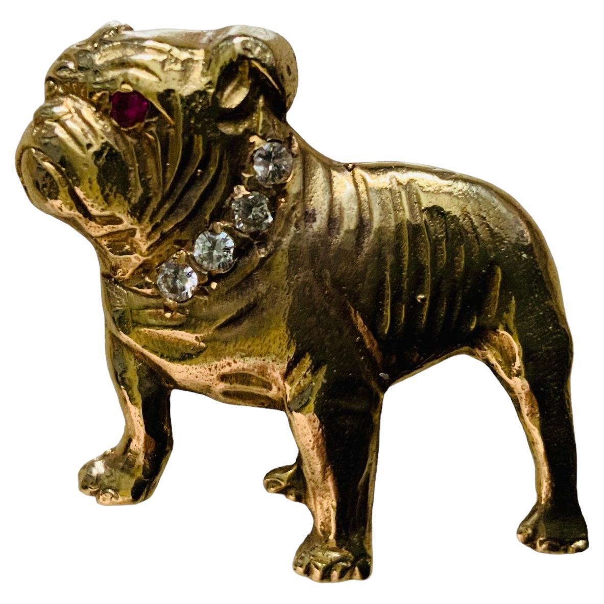 Dies ist ein 14K Gelbgold, Diamant und Rubin Bulldog Pin / Brosche. Es zeigt eine aufrecht stehende Bulldogge, die mit einer Halskette aus vier Diamanten in Pflasterfassung und einem Rubinauge in der gleichen Fassung geschmückt ist.
