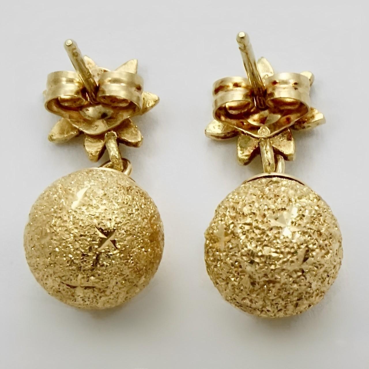 Lovely 14K gold earrings featuring textured balls with a diamond cut design dropping from diamond cut flowers. Length 1.8 cm / .7 inch and the ball is 8 mm / .3 inch.

This is a beautiful pair of gold earrings with movement and sparkle.