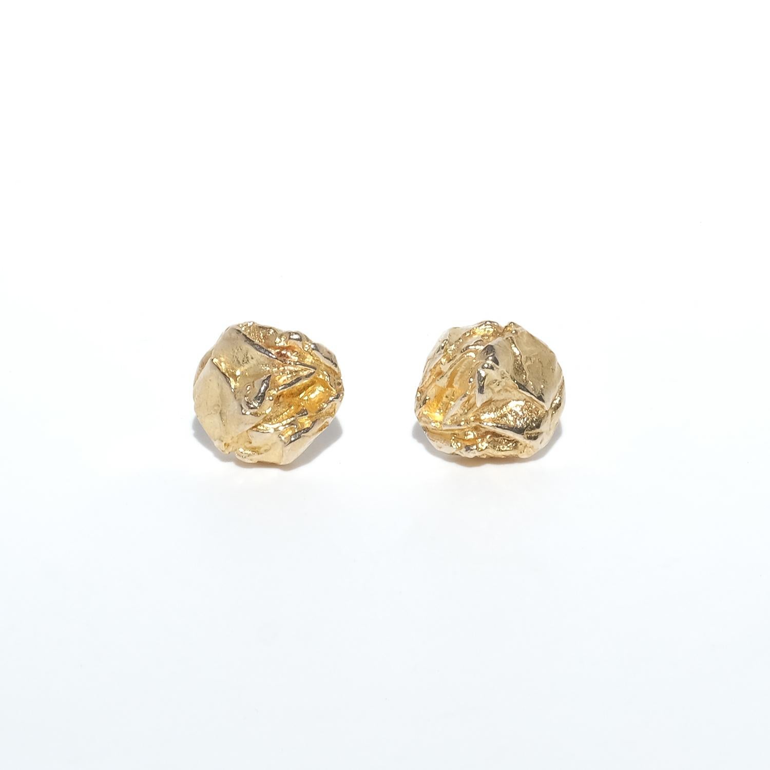 These 14-karat gold earrings, known as Nuggets, feature a textured, organic shape that resembles molten gold, giving them a distinctive, artistic appearance. The bright golden hue enhances their sculptural design, catching and reflecting light