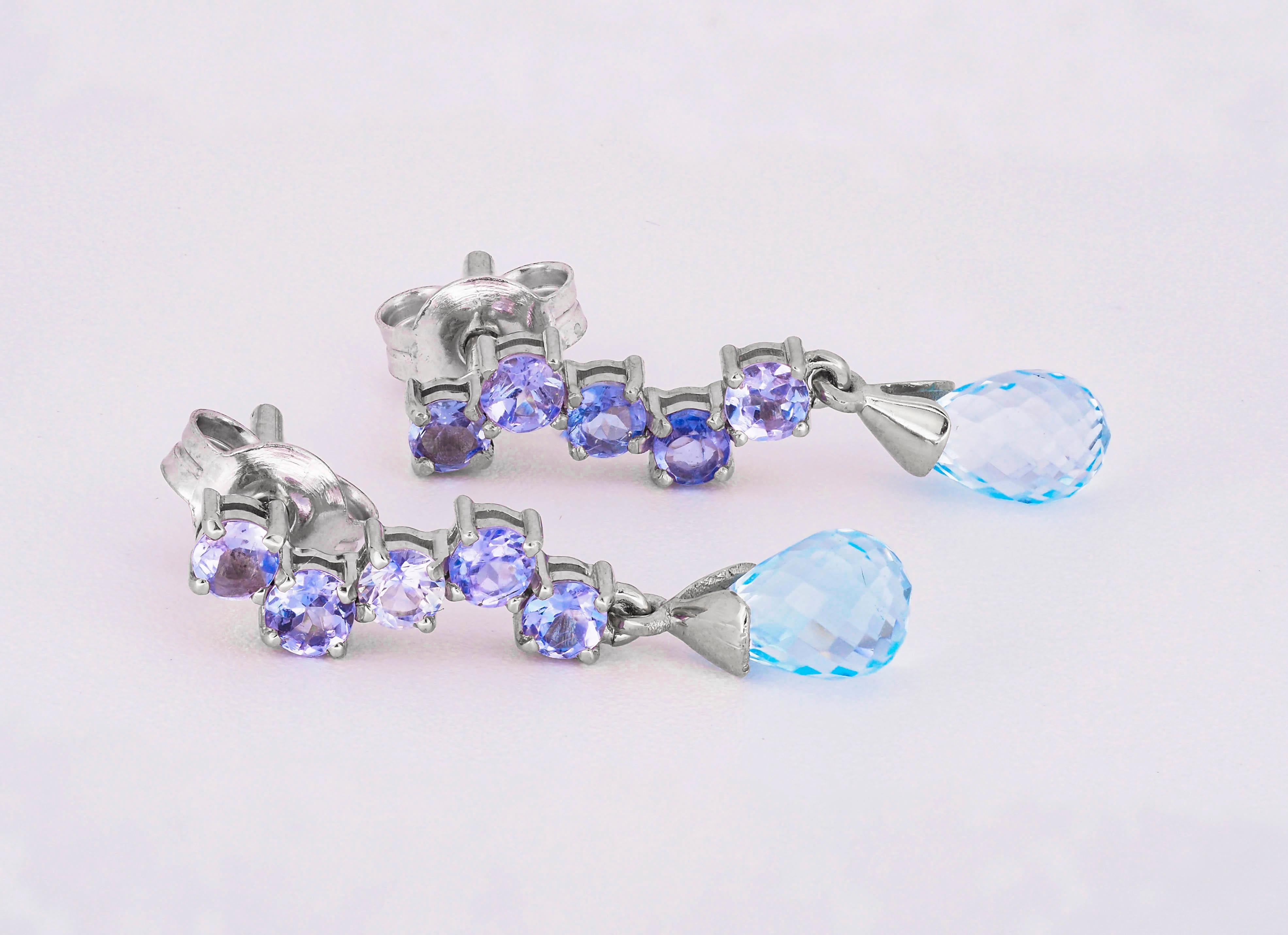 14 kt solid gold earrings with natural topazes and tanzanites
Total weight: 2.20 g.
Size: 22 x 5 mm.

Central stones: Natural topaz 
Weight: approx 2.00 ct total, 2 pieces, cut - briolettes
Color: blue, clarity - transparent with inclusions
Side