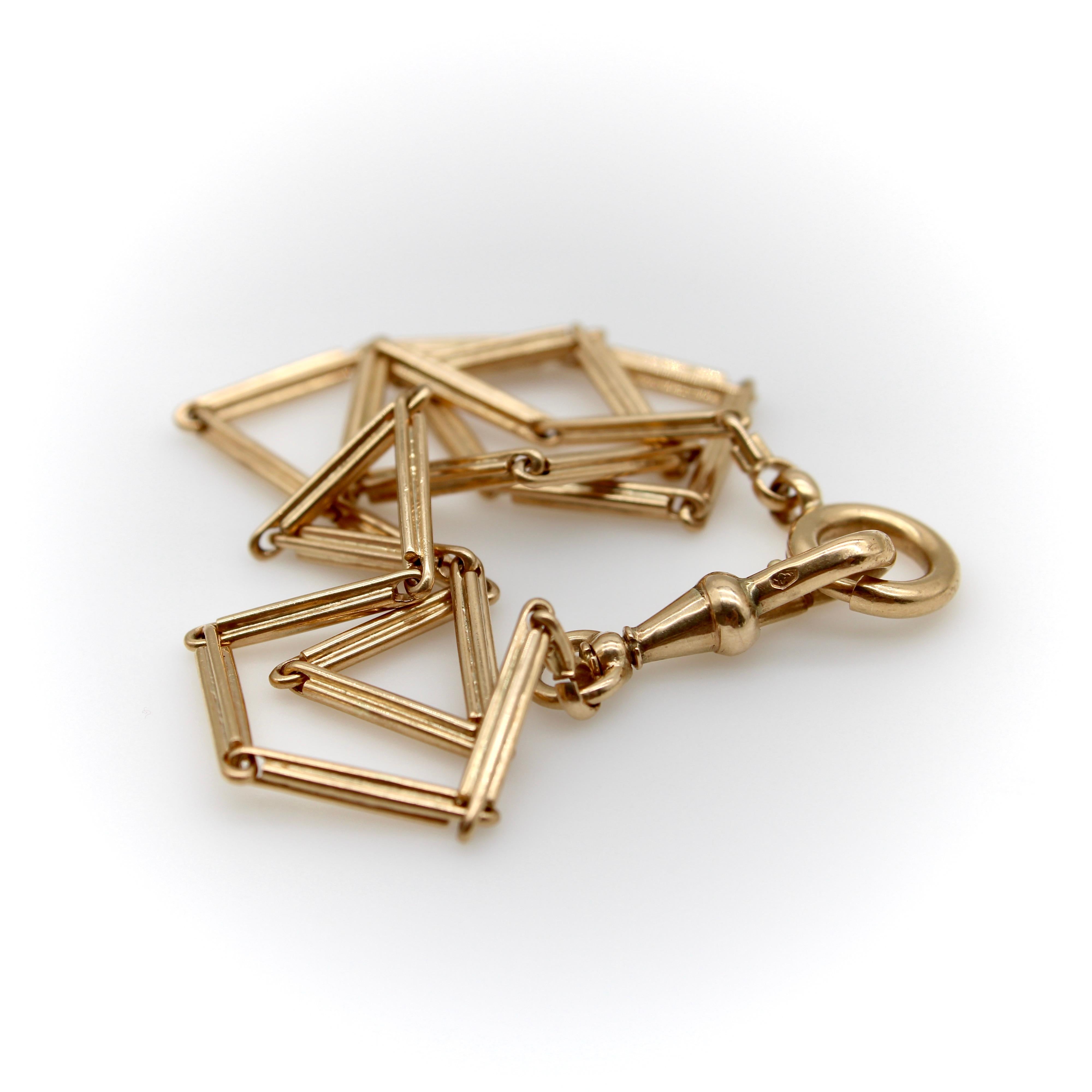 This 14k gold Edwardian watch chain consists of bar links that come together to form a solid, slinky chain. Each link has four linear lines that are interlocked and delineate the chain. The chain culminates in a dog clip, as well as a medium sized