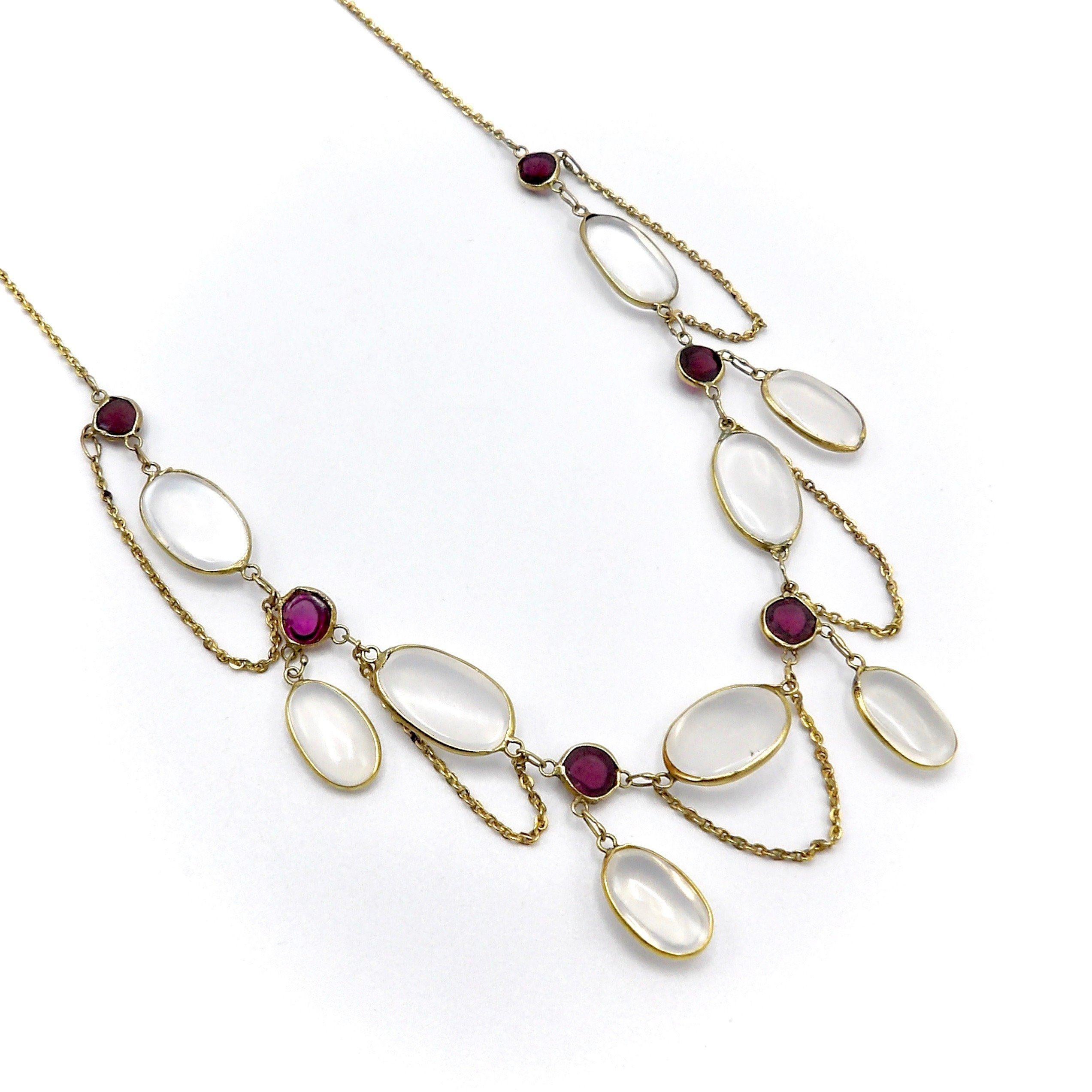 This gorgeous festoon necklace has a soft and delicate arrangement of moonstone and garnet cabochons, favorites of the Edwardian era. Feminine and romantic, the necklace drapes to create gorgeous curved lines around the neck. Five oval moonstone