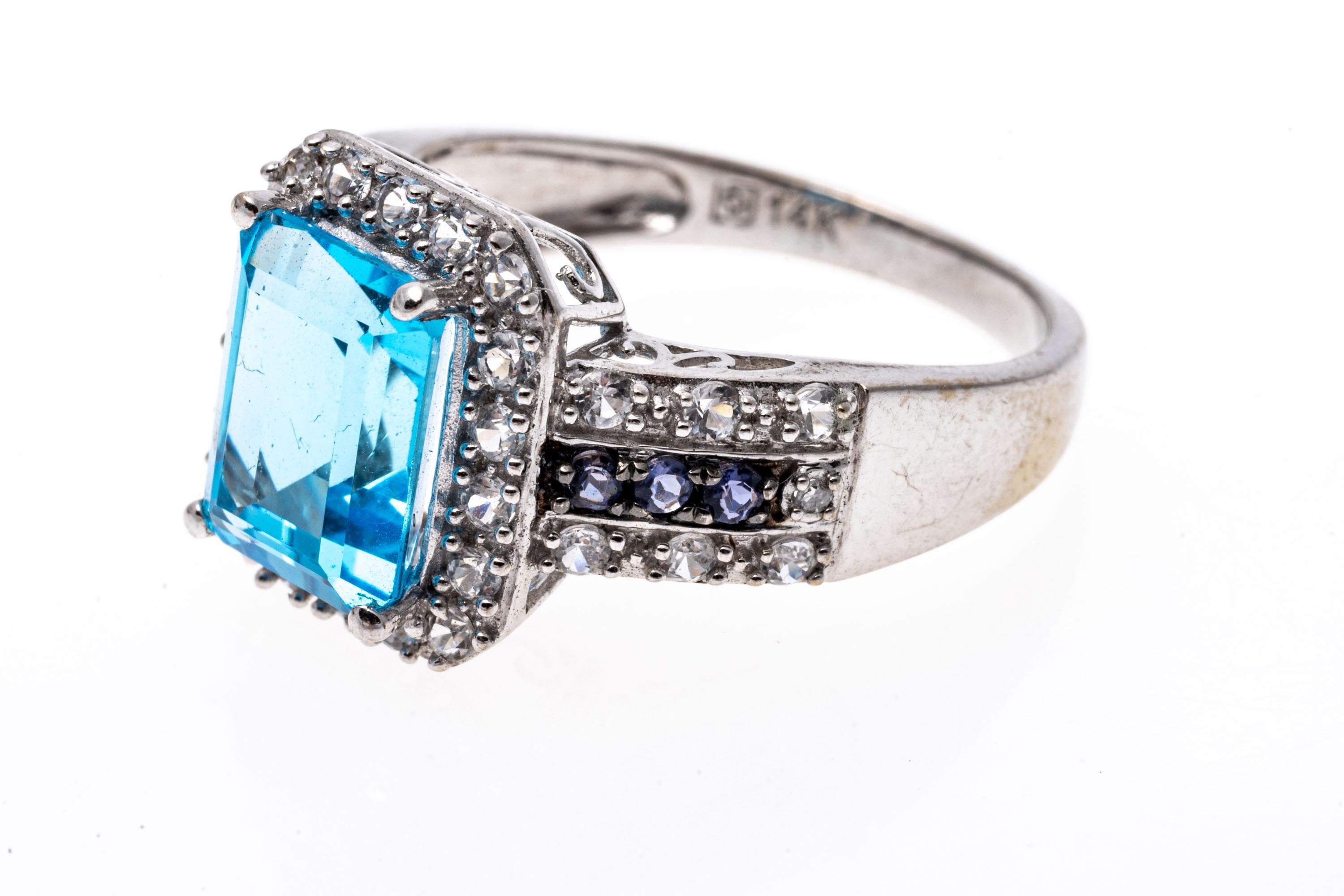 This bold ring displays a beautiful emerald cut medium blue color blue topaz, approximately 2.45 CTS. Framing the blue topaz, and flanking the center are round faceted white topaz stones.
Marks: 14k
Dimensions: 3/4