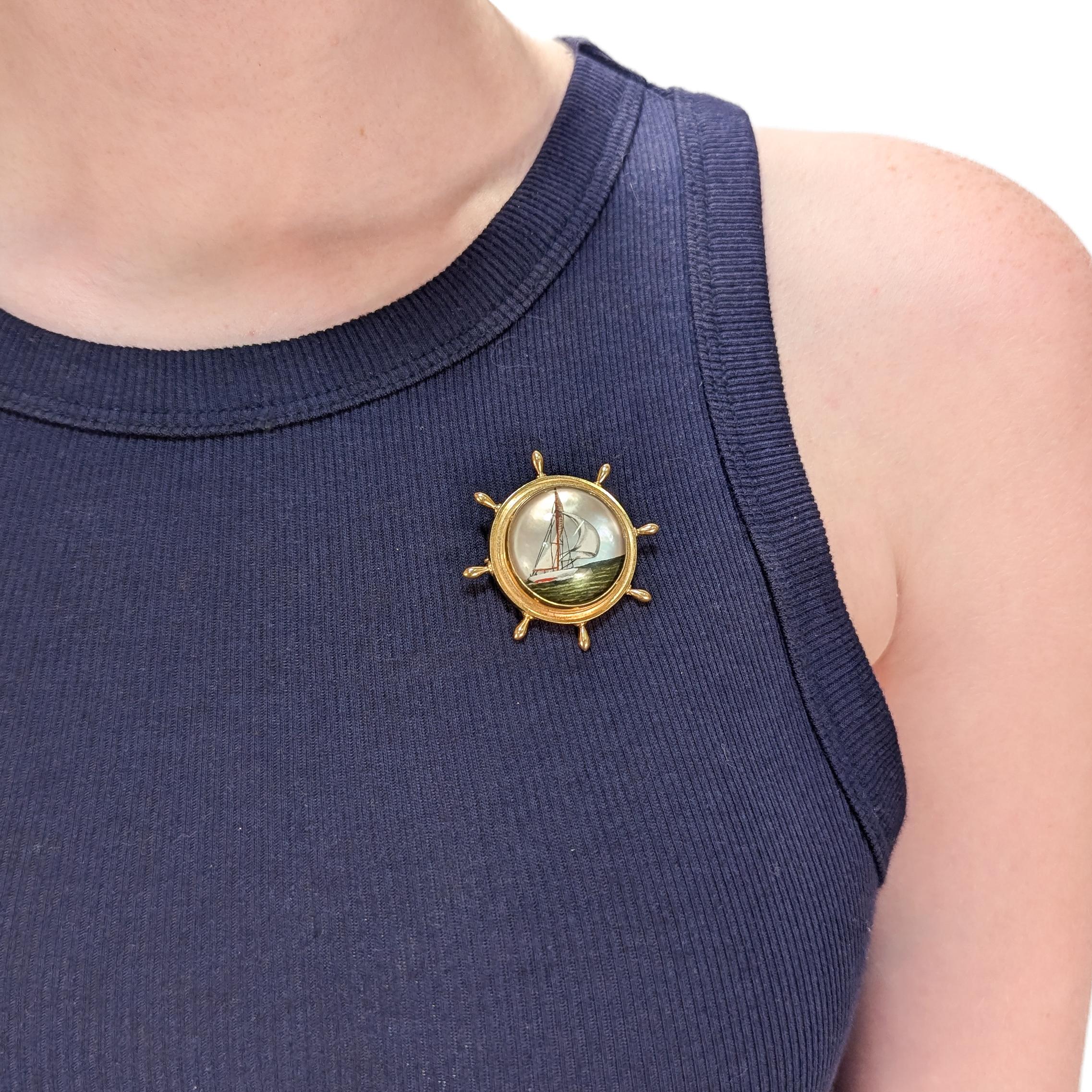 Broche antiguo de oro y cristal de Essex.

En oro amarillo de 14 quilates.

En forma de rueda de barco con un gran cabujón de cristal de Essex en el centro decorado con un velero estilo balandra en el mar sobre un fondo de nácar.

Asegurado con un