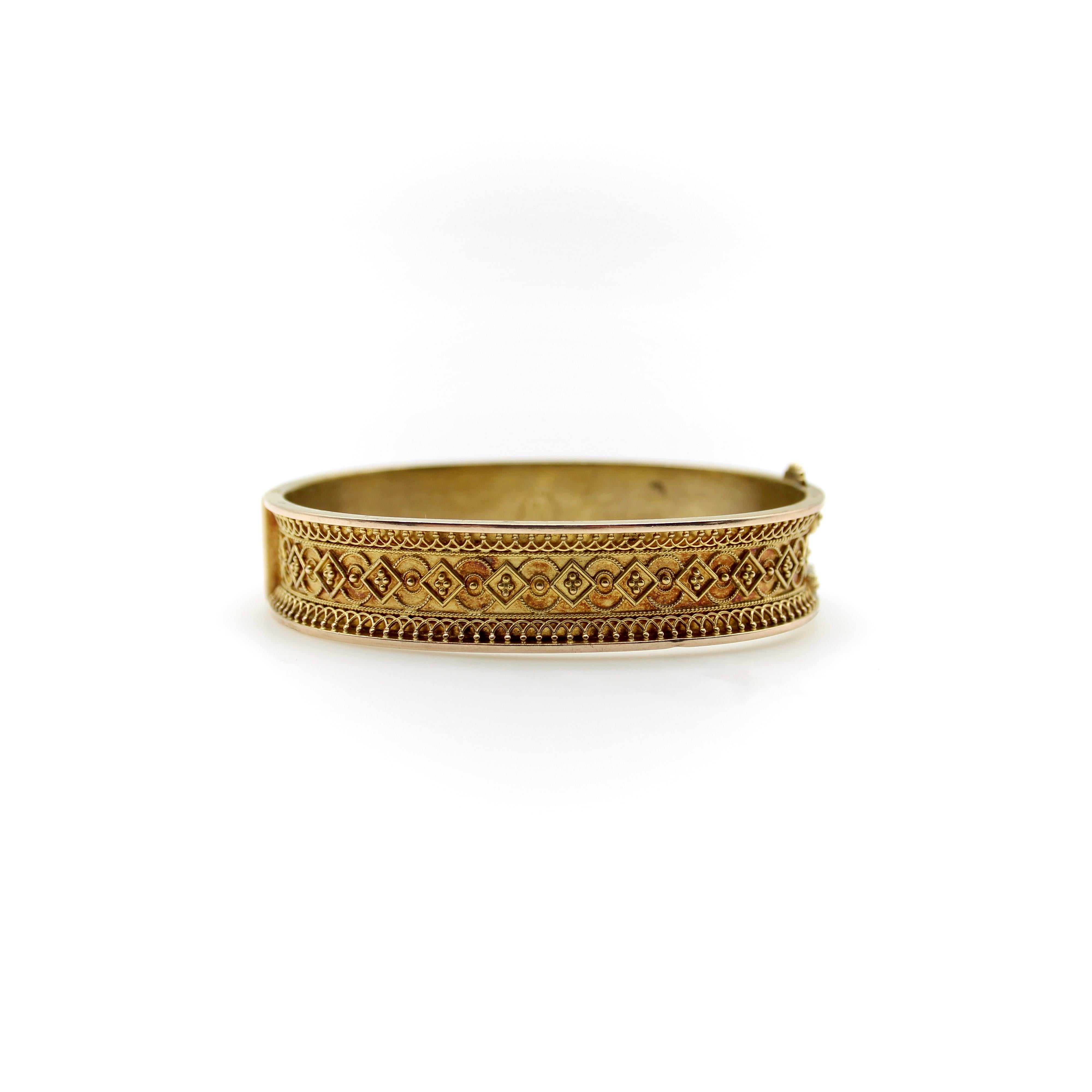 This beautiful 14k gold bracelet features intricate Etruscan Revival wirework, with twisted gold wire, a repeating motif of squares and circles, and swooping designs along the top and bottom of the band. The gold has a gorgeous patina that gives it