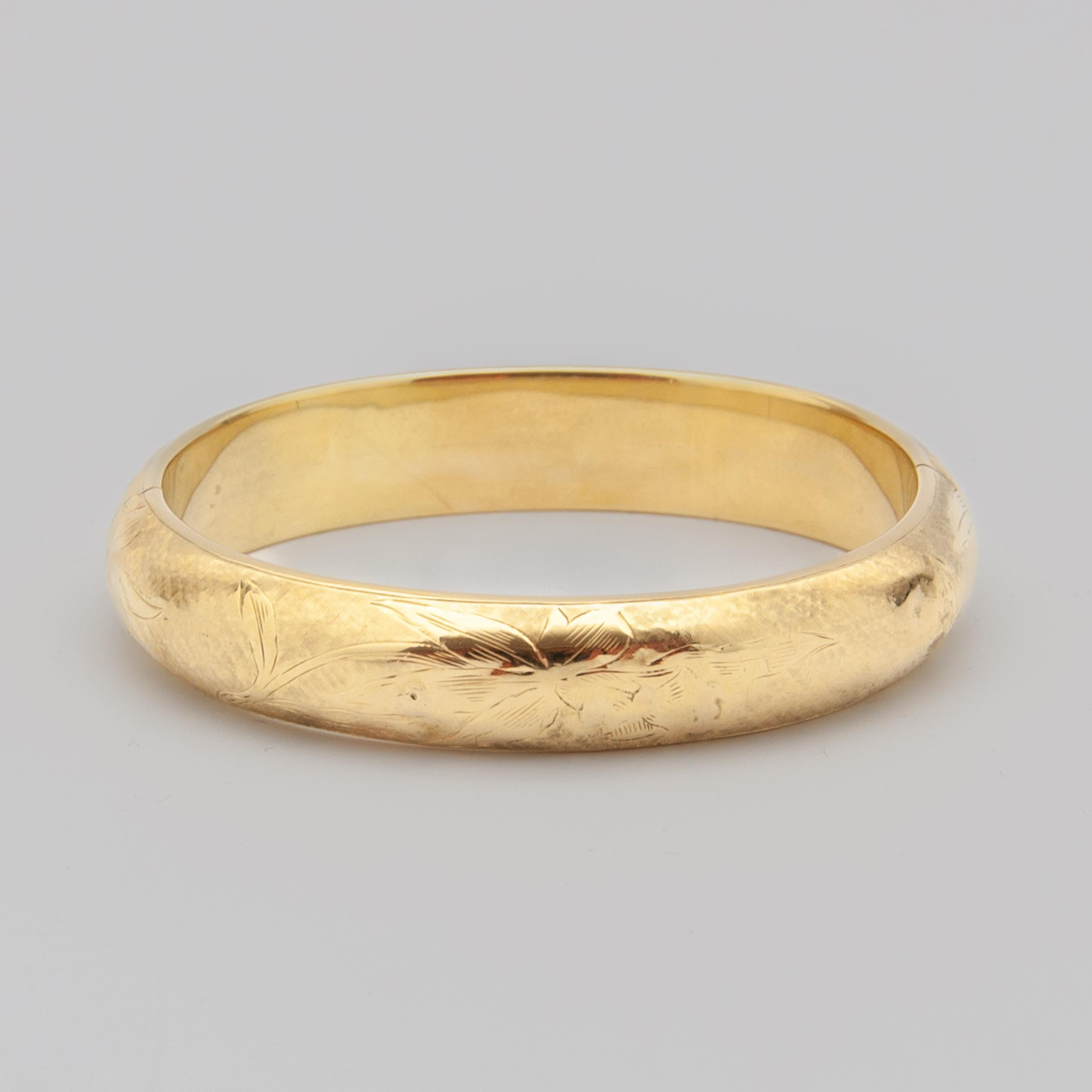 A gorgeous 14 karat gold floral engraved bangle bracelet. The gold bracelet is beautifully satined on its surface and engraved with a floral design. The bangle is hinged on the side and closes with a secure push clasp. This stunning bangle bracelet
