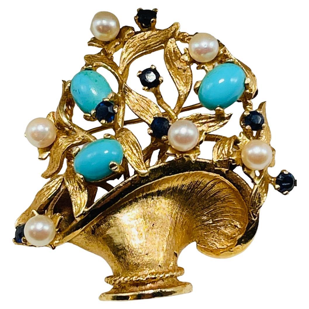 This is a 14K yellow gold gemstones and pearls flower’s basket brooch. It depicts a large basket with branches of flowers and leaves embellished with seven round cut sapphires, six round pearls and three oval turquoises in prong setting. The brooch