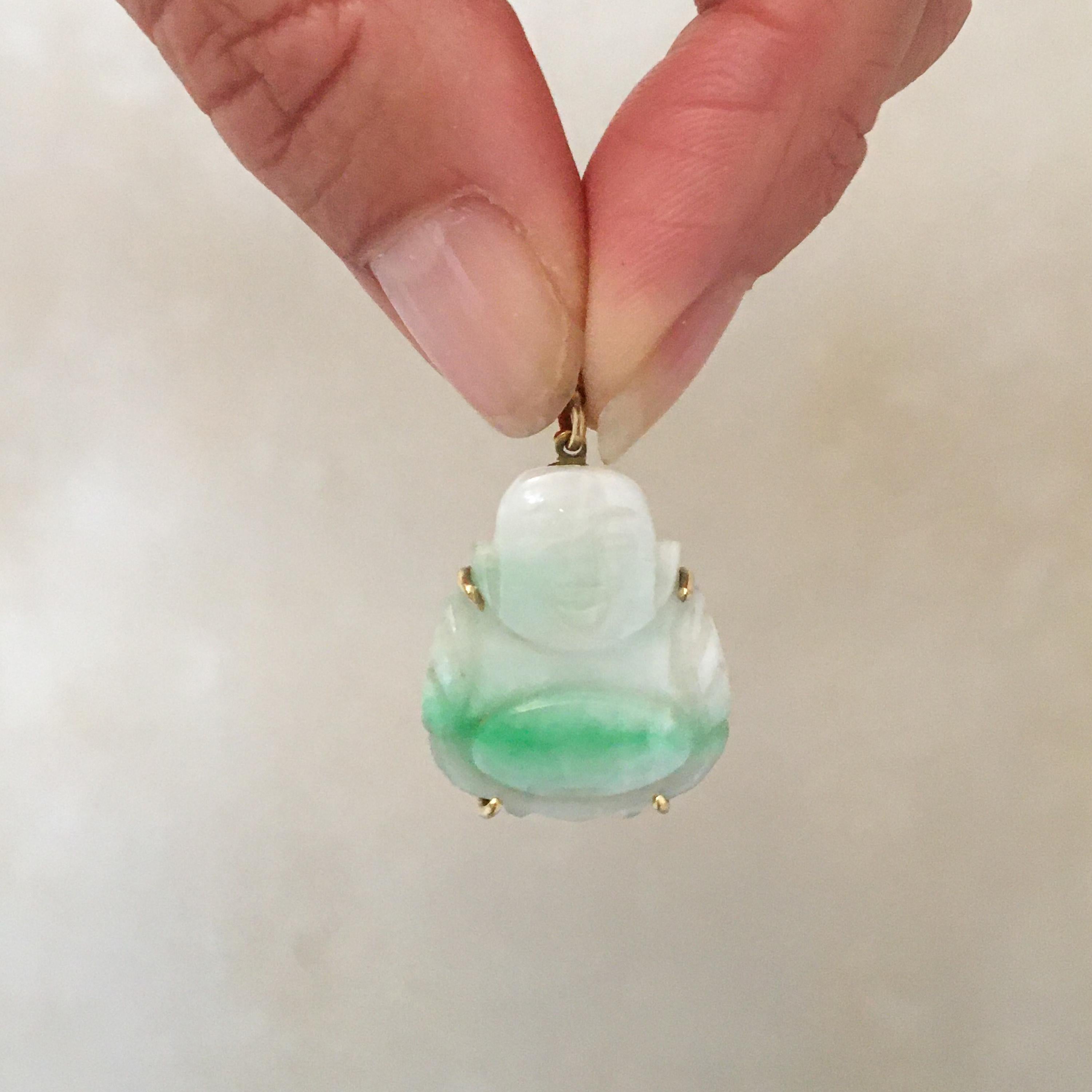 A green and white jade pendant carved in the shape of a smiling seated belly buddha. This pendant is made of jade with a green in white fade color tone. The mounting and eyelet of this lovely buddha is made of 14 karat gold. 

The jade pendant is in