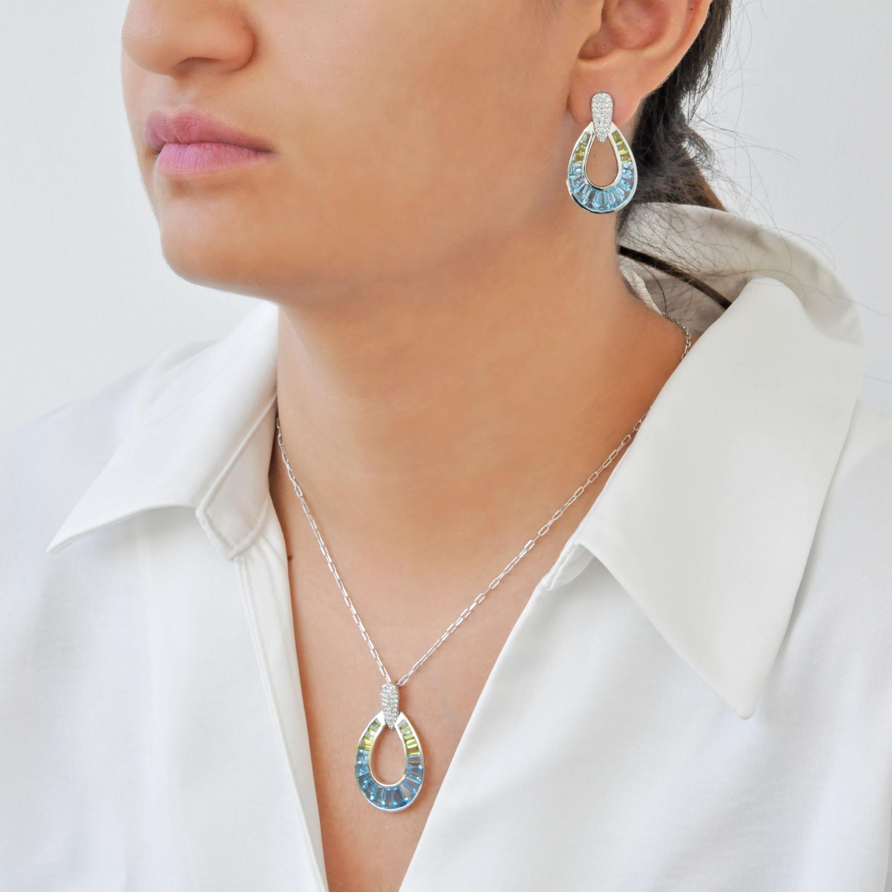 Step into a world of vivid elegance with this 14K gold hand-crafted earring and pendant set, featuring a luminous arrangement of tapered baguette-cut blue topaz and peridot gemstones, seamlessly channel set to form a striking gradient of cool blues