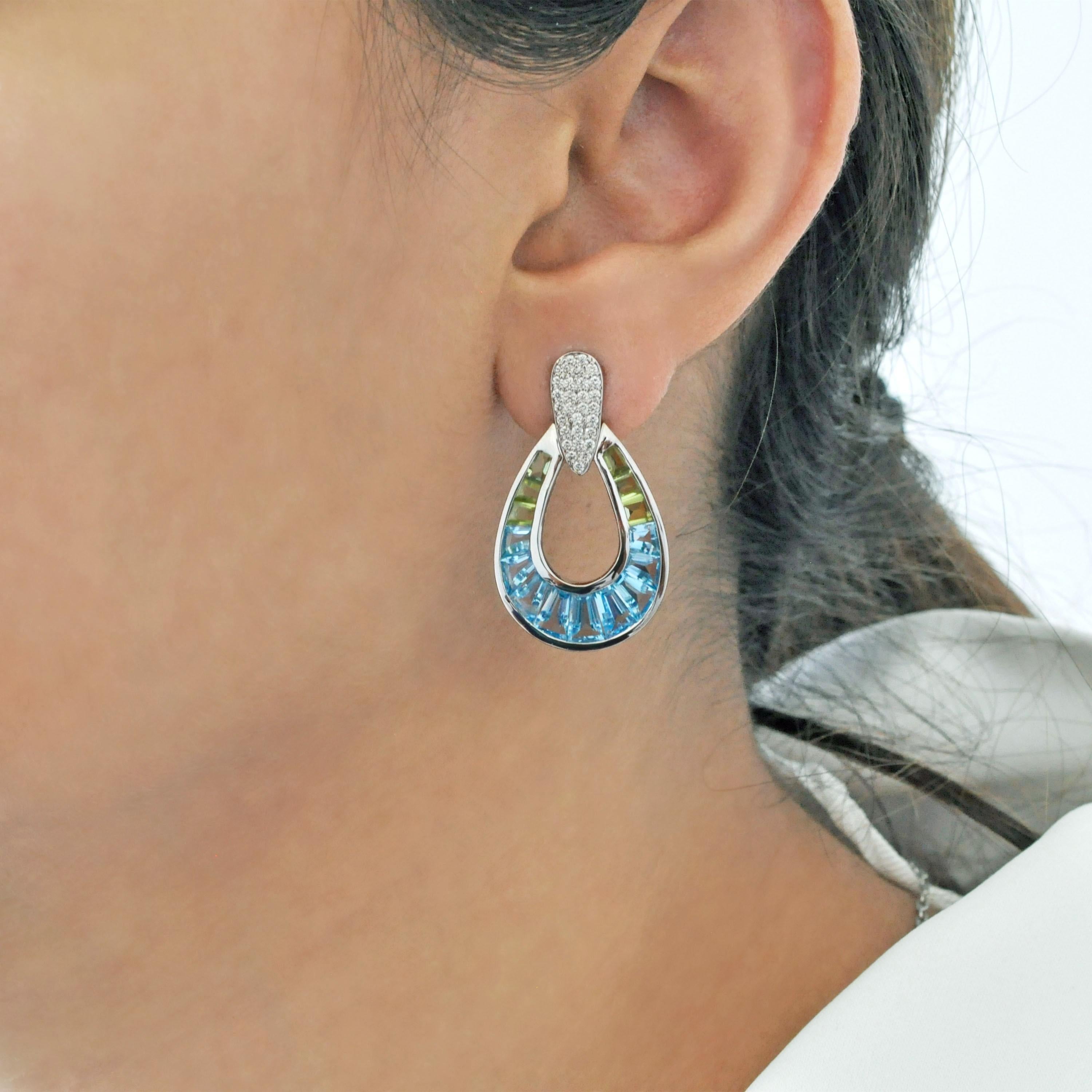 14K gold hand-crafted dangling drop earrings feature a brilliant fusion of taper baguette-cut blue topaz and peridot gemstones, channel set with precision to create a pleasant, colorful cascade of light.

Each earring showcases a dazzling drop