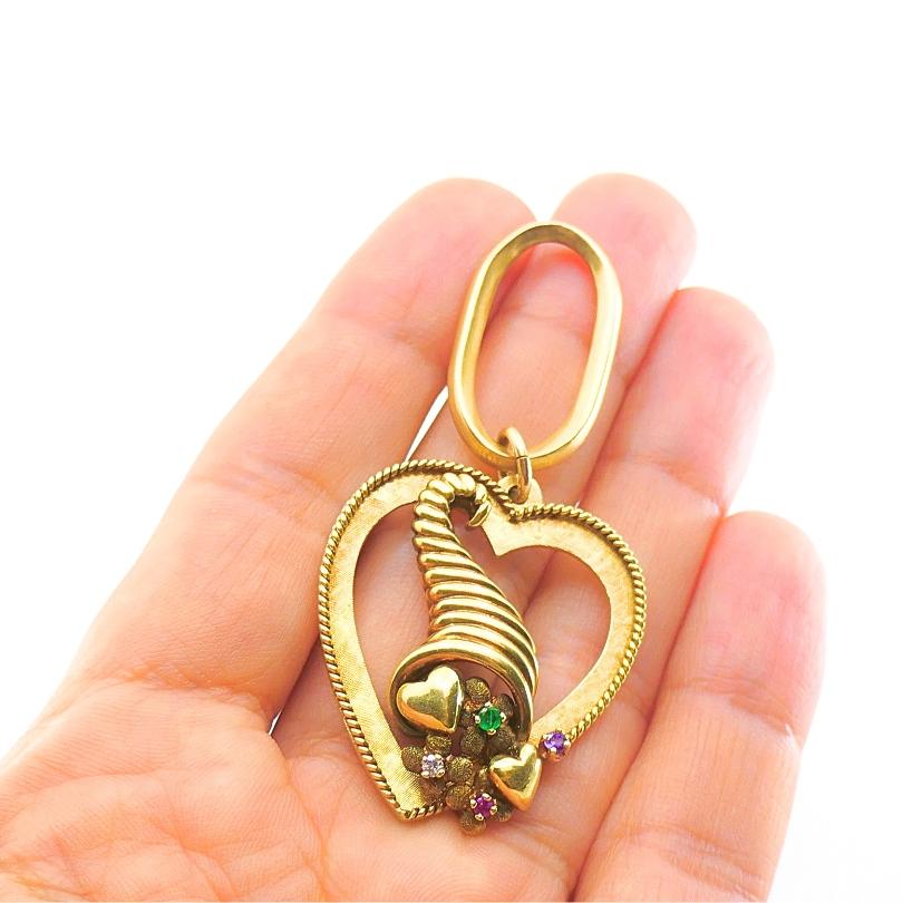 Un ciondolo a forma di cuore in oro 14k, con il disegno della cornucopia al centro.
Questo pezzo vintage traforato mostra un bellissimo mix di cinque tecniche di lavorazione dell'oro.
Il cuore strutturato è incorniciato da un disegno a forma di