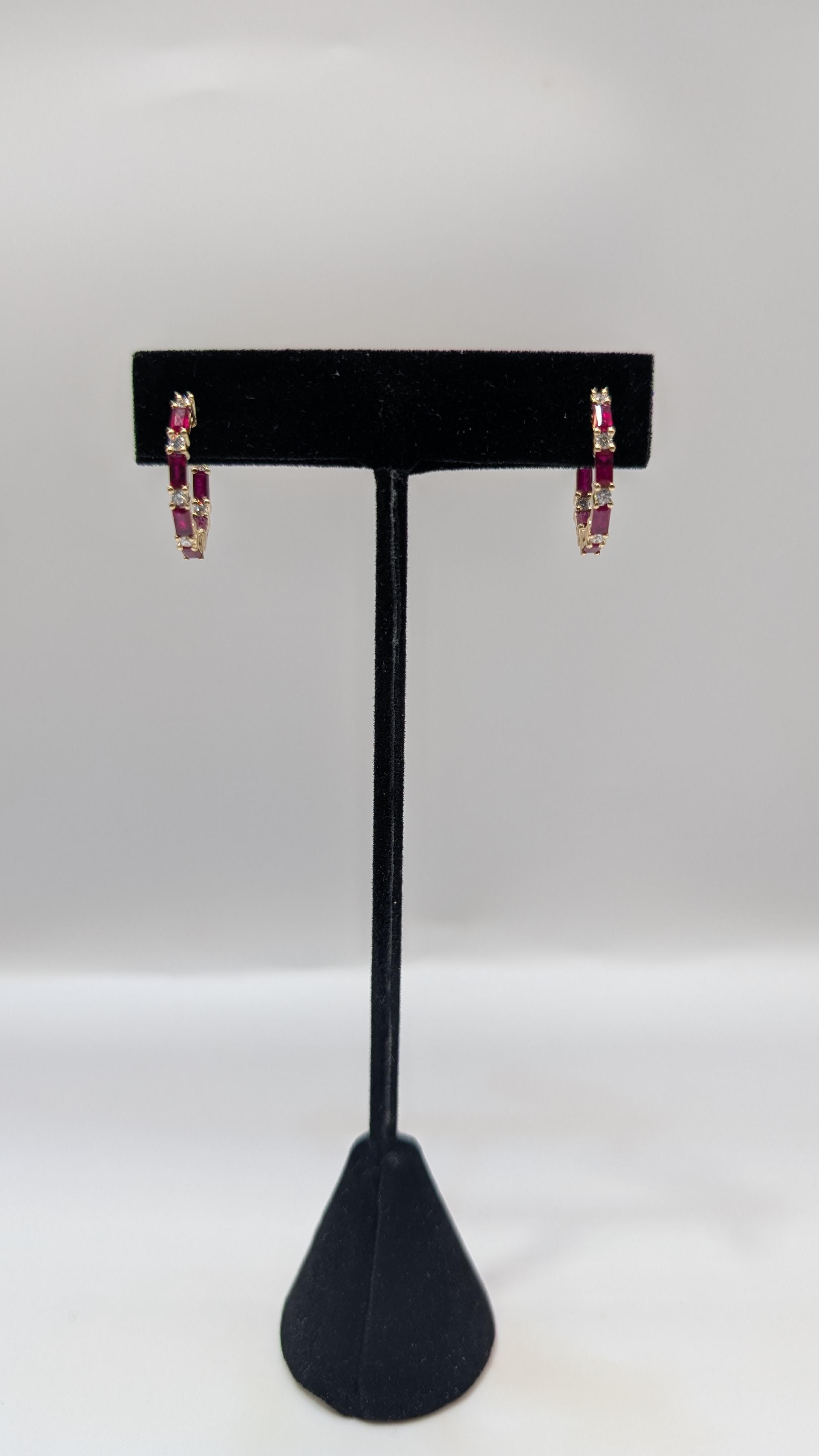 These elegant 14k yellow gold hoop earrings feature a stunning combination of emerald cut rubies and round cut diamonds. The rubies, with their red hue are expertly cut into an emerald shape, adding sophistication and sparkle. Interspersed between