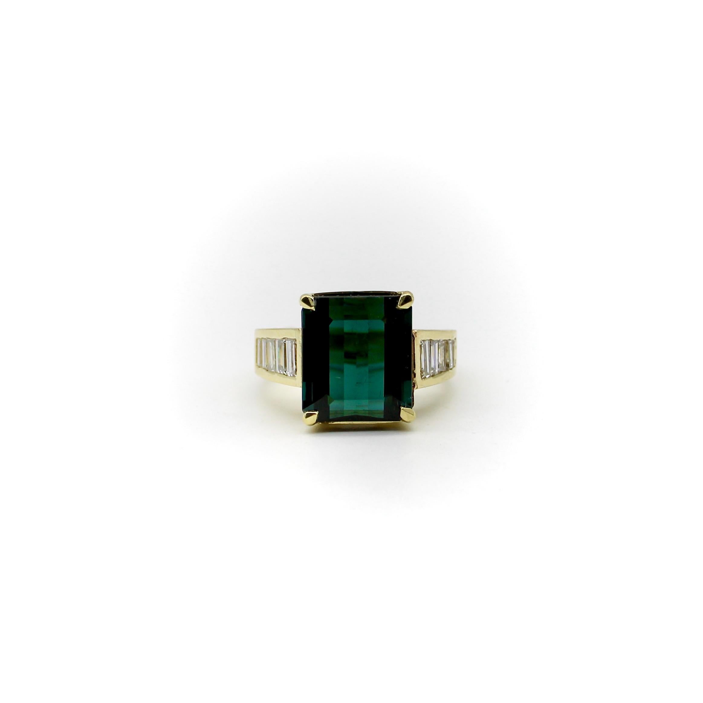 This gorgeous 14k gold cocktail ring features a deeply saturated blue-green Indicolite Tourmaline, with rows of channel set baguette diamonds down each side of the ring. The rectangular gemstone is large, with a stunning presence on the hand, and is