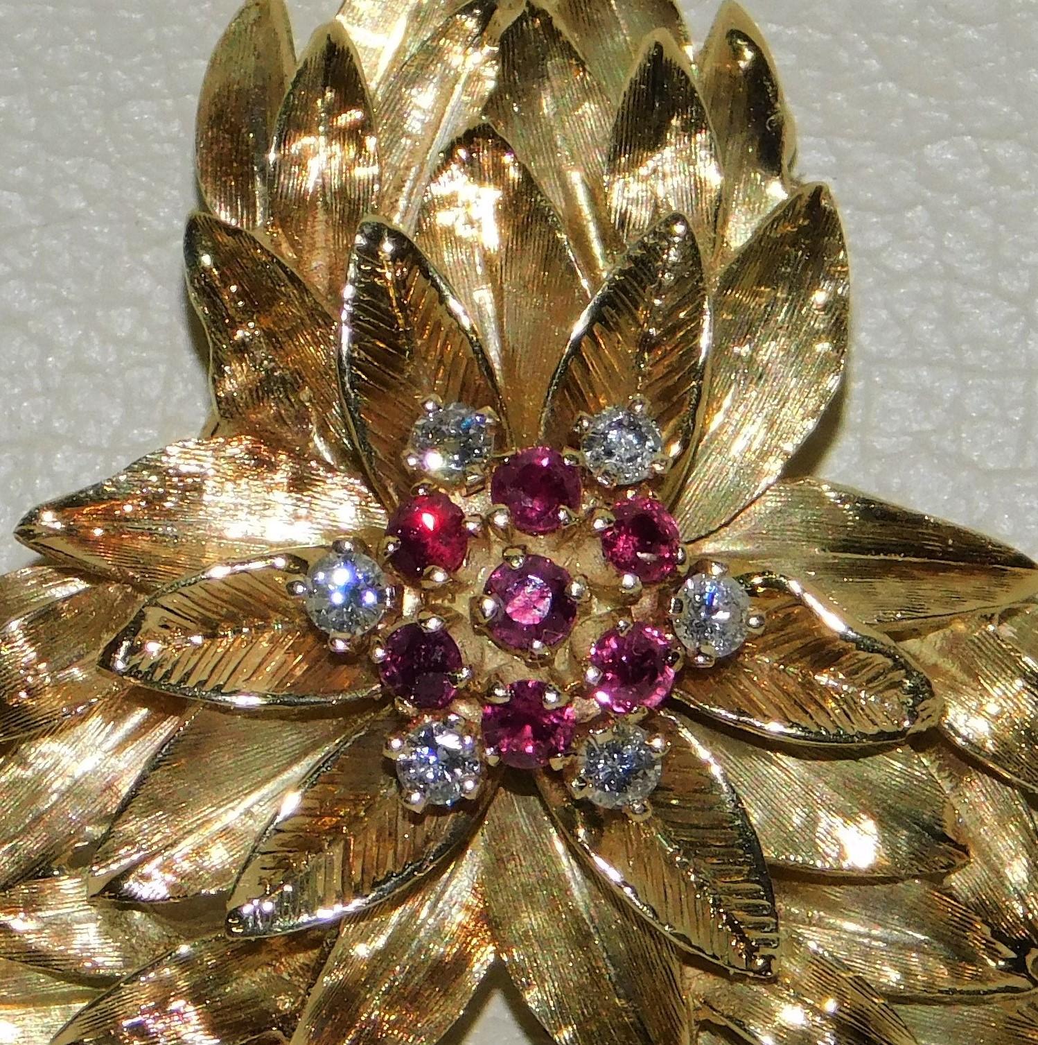 Stamped 14KT yellow gold ladies hand assembled brooch with a bright polish and textured finish in very good condition with a leafy floral design.  Centre of the brooch is set with round brilliant cut rubies and diamonds.  Brooch measures